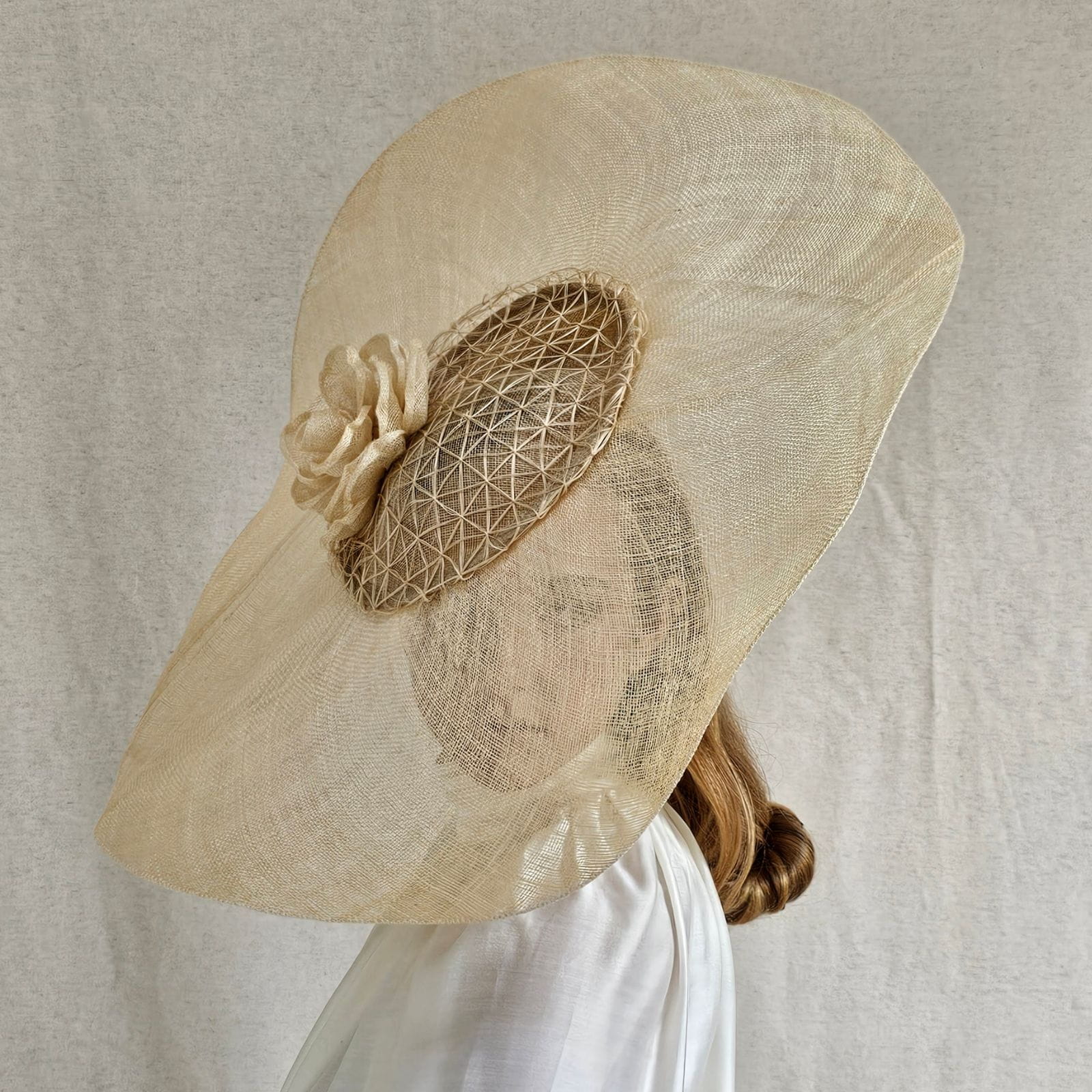 Model wearing natural sinamay Ascot disc hat with mesh veil and sculptural rose detail.
