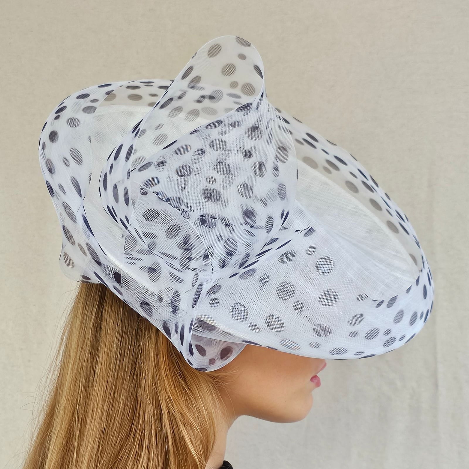 White ascot disc hat with black spotted crin swirl embellishment, side view.