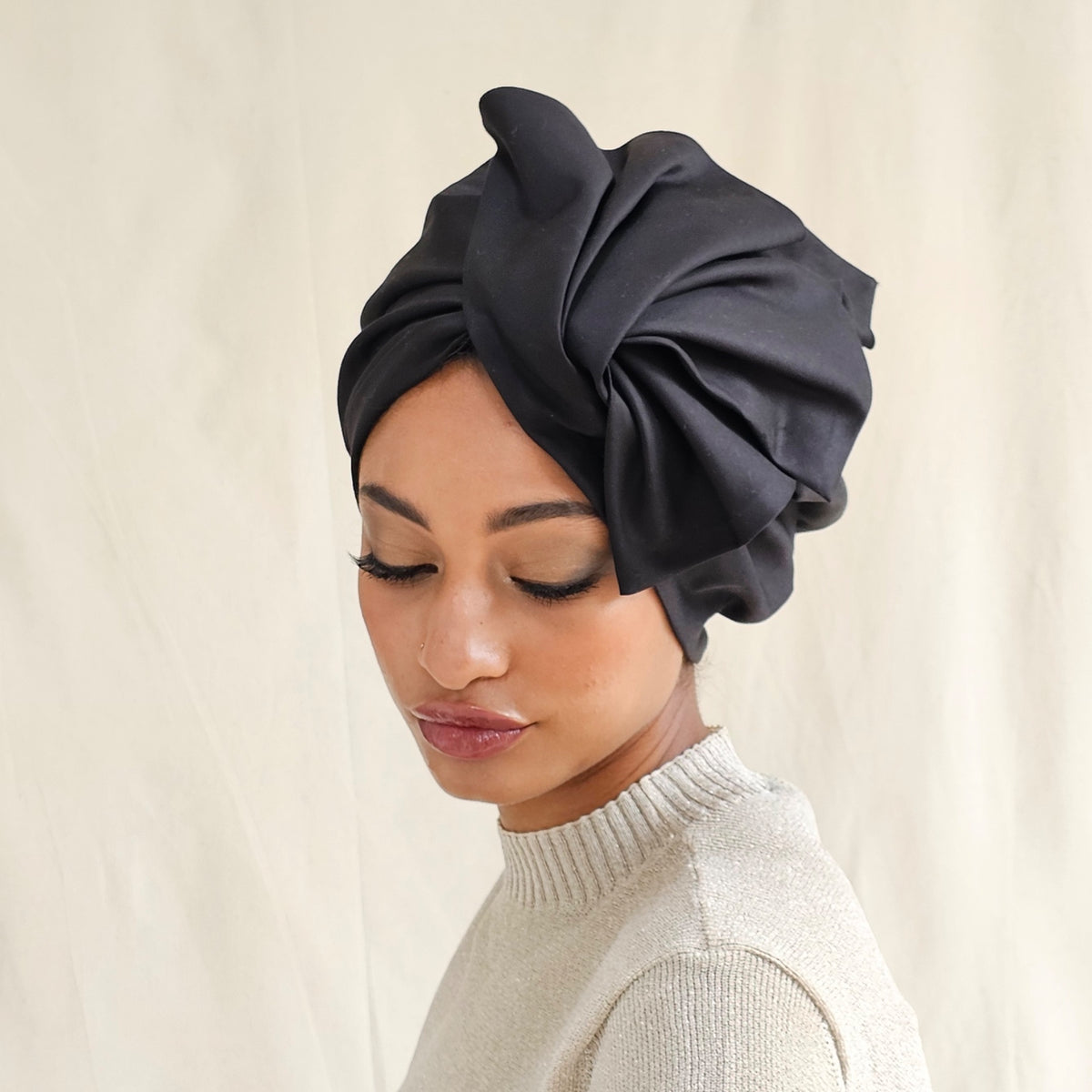 Black cotton turban with dramatic fold sculpting, side view on model.
