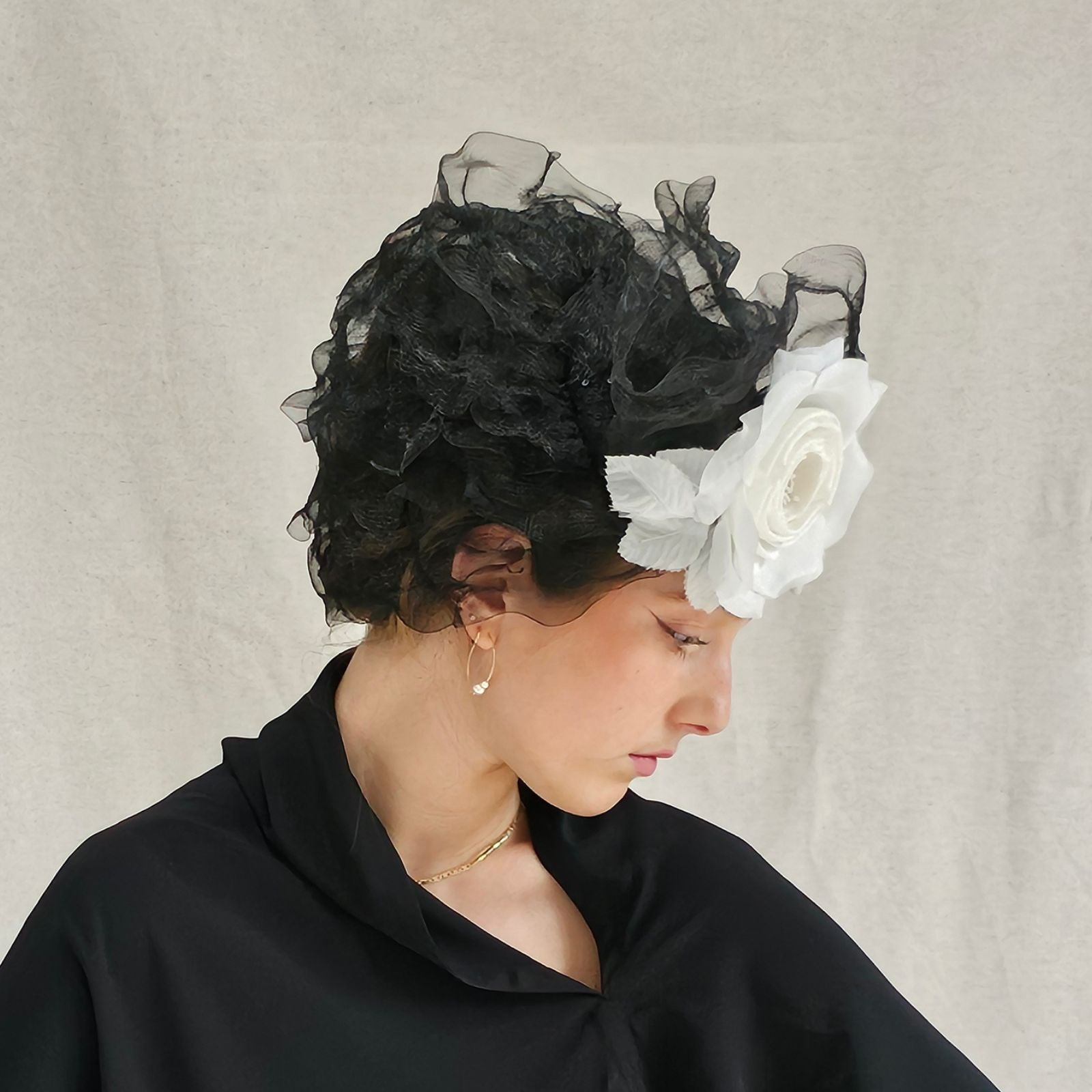 Black turban hat with elegant crin ruffle swirls and dramatic white flower, angle view.