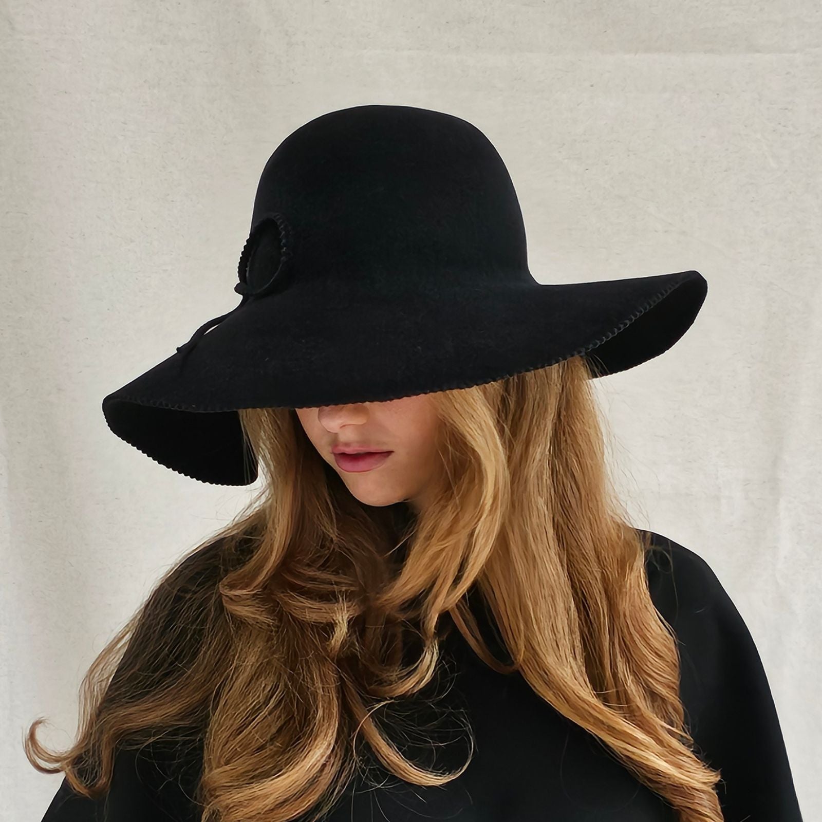 Black felt 1970s hat with elegant bow embellishment, left view.