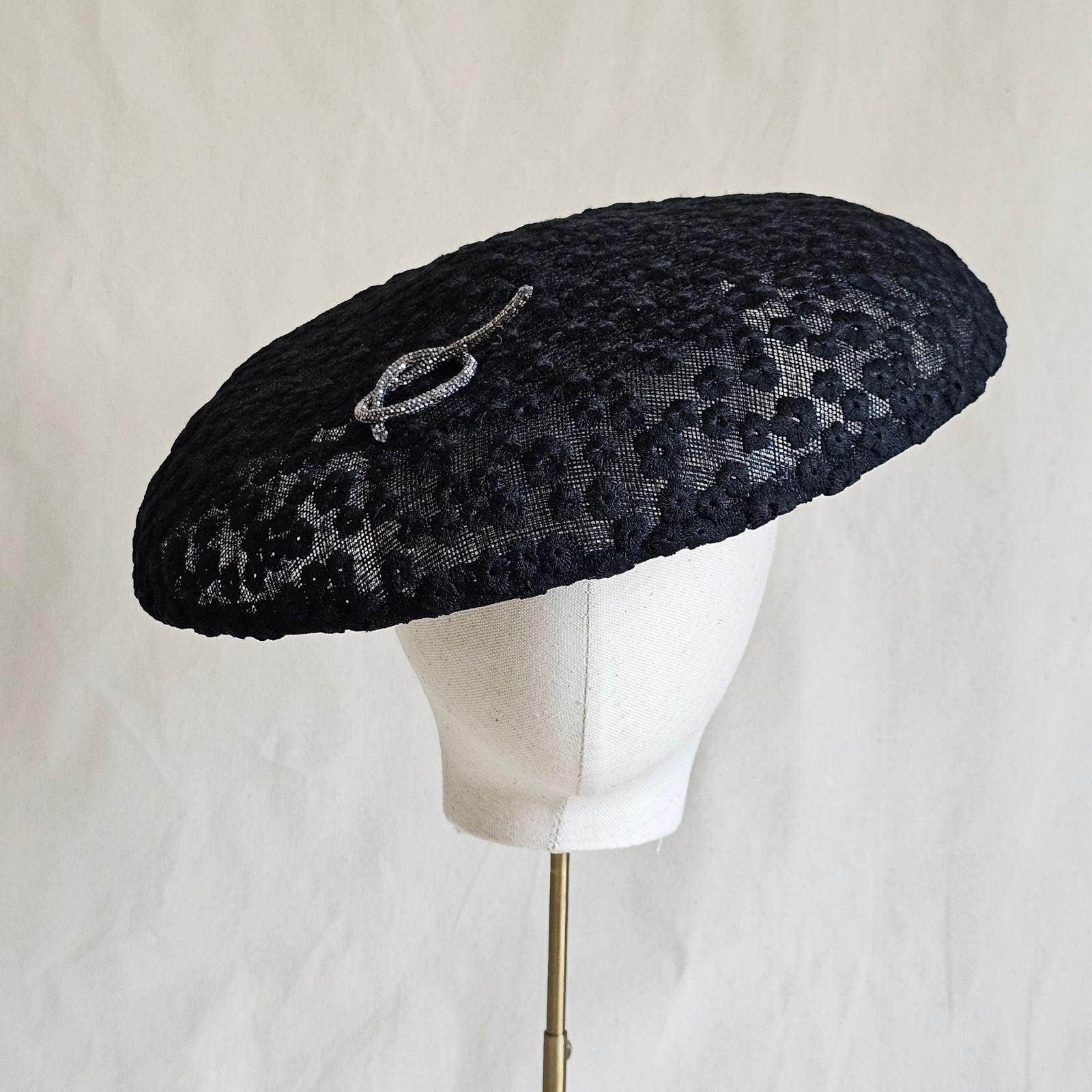 Black disc hat with beautiful flower lace and silver pretzel knot embellishment, front view.