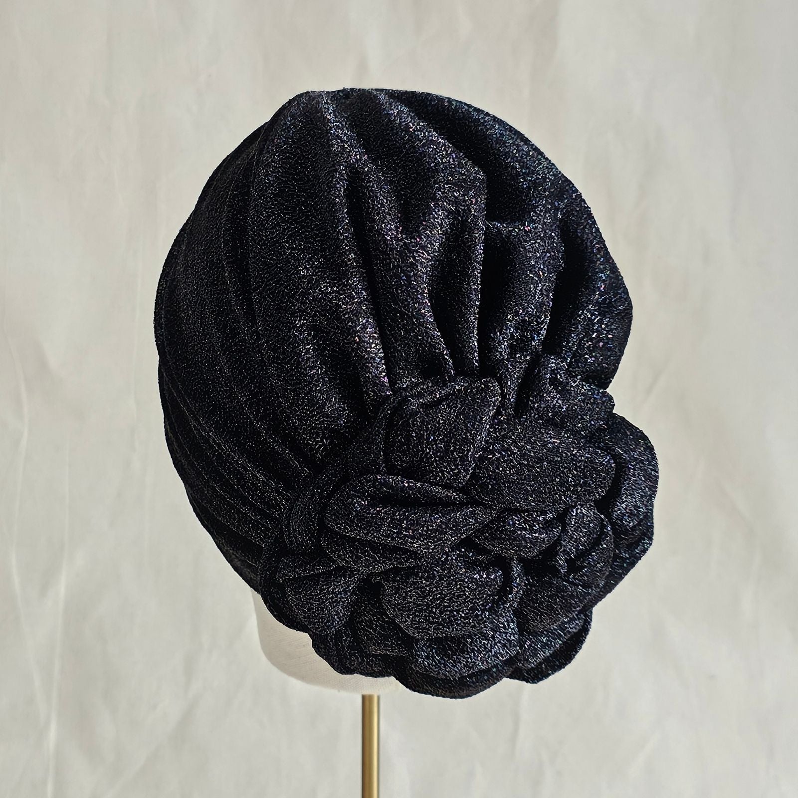 Black lurex turban loosely gathered into intricate plaited rose, back view.