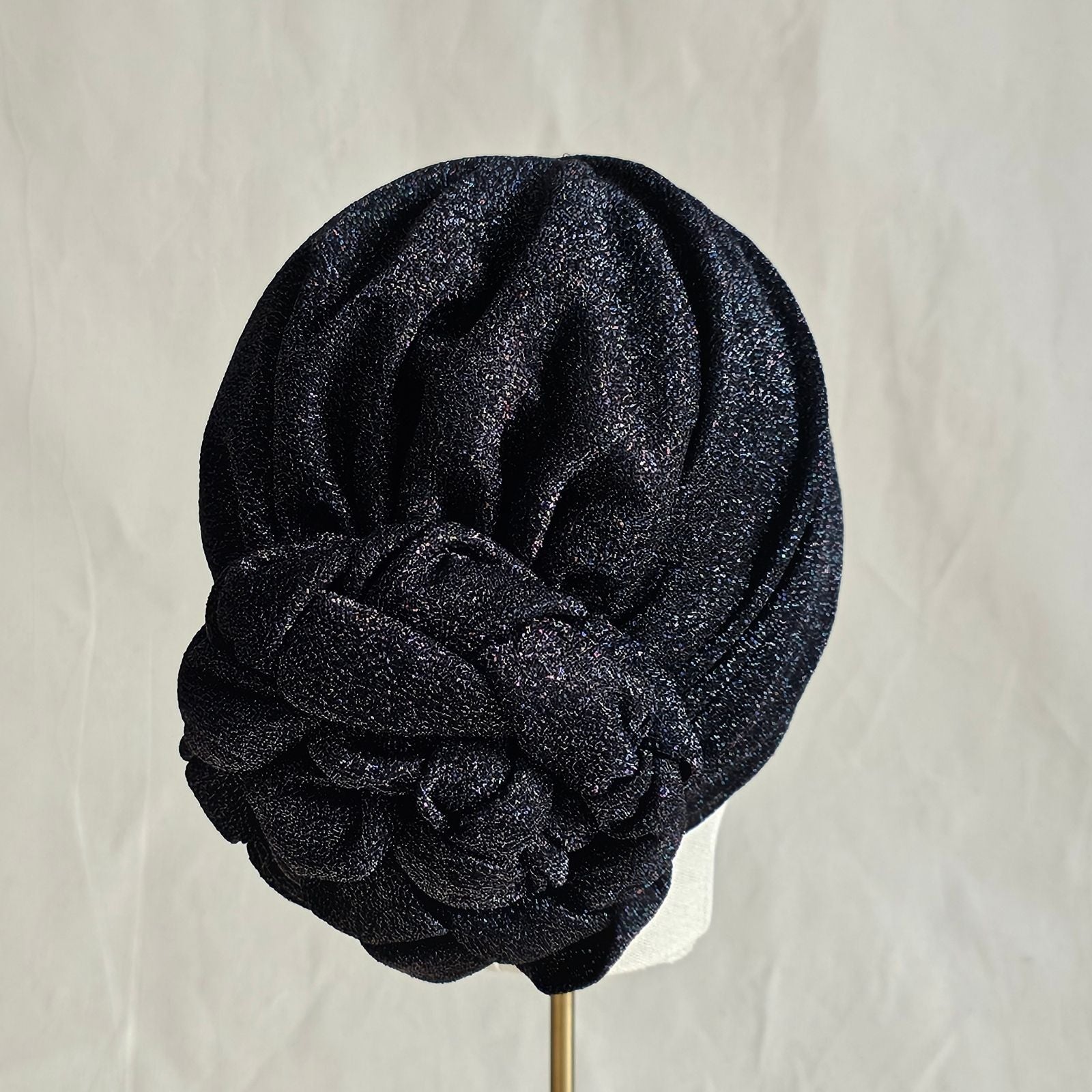 Black lurex turban loosely gathered into intricately plaited rose, back left view.