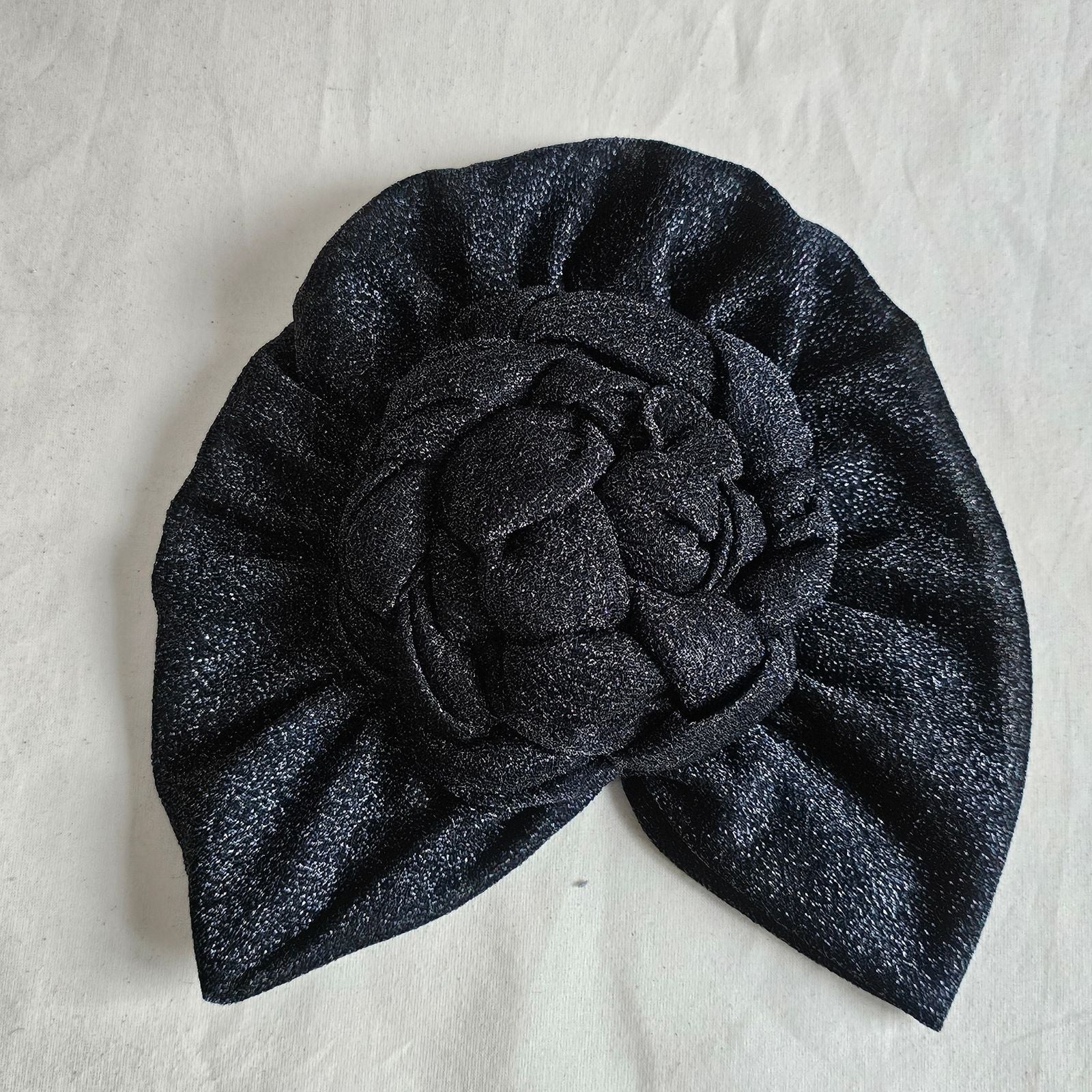 Black lurex turban loosely gathered into an intricately plaited rose, top view.
