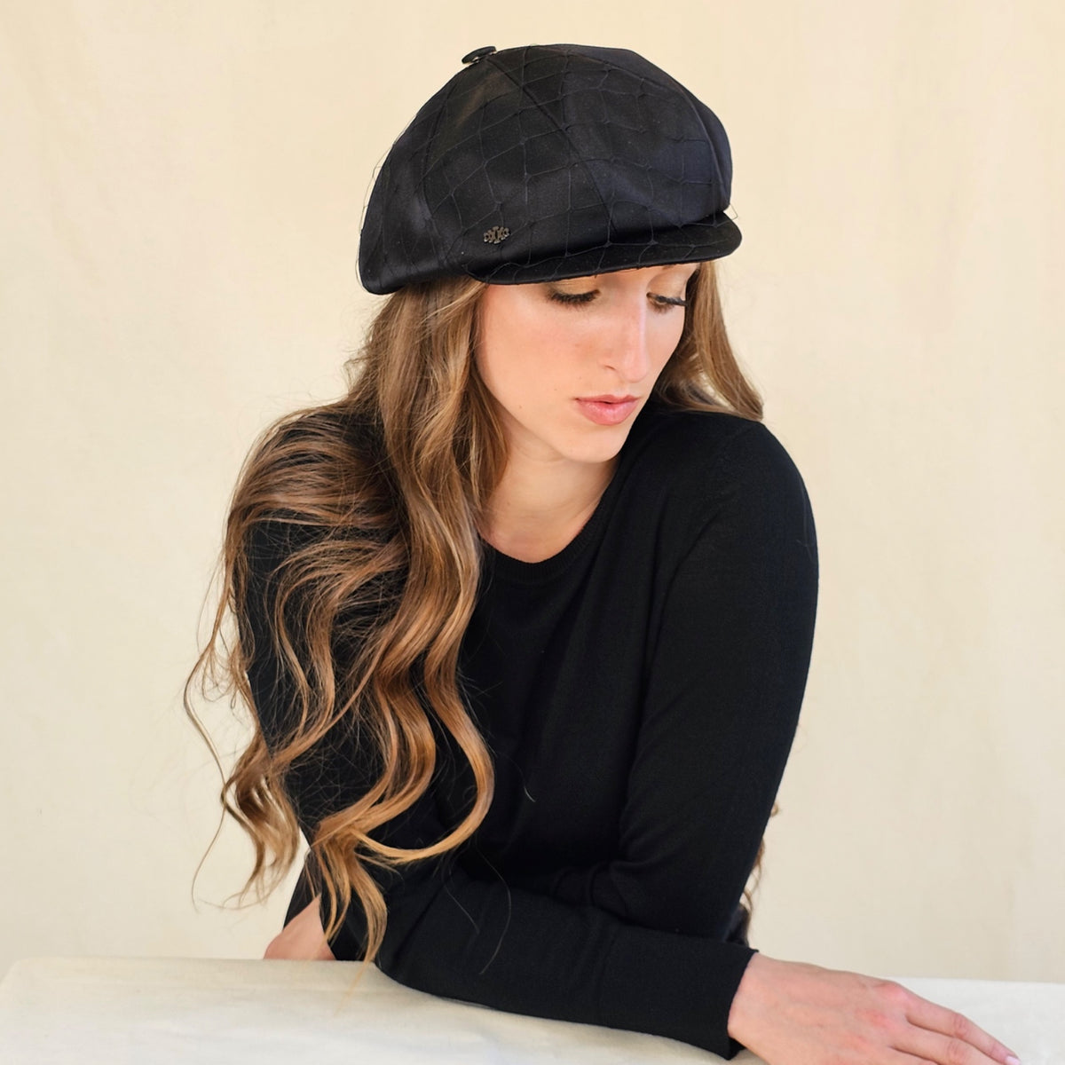 Black silk satin baker boy cap with veil, model looking down.