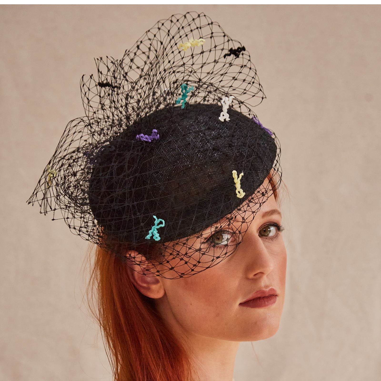 Black sinamay beret with intricate black veiling and multicolour bow detailing, angle view.
