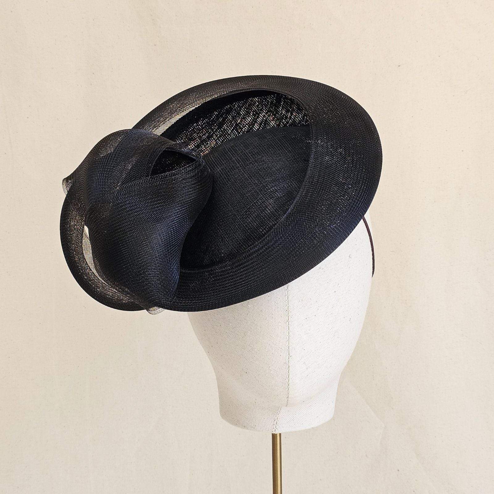 Black straw disc hat with sculptural crin knot, front view.