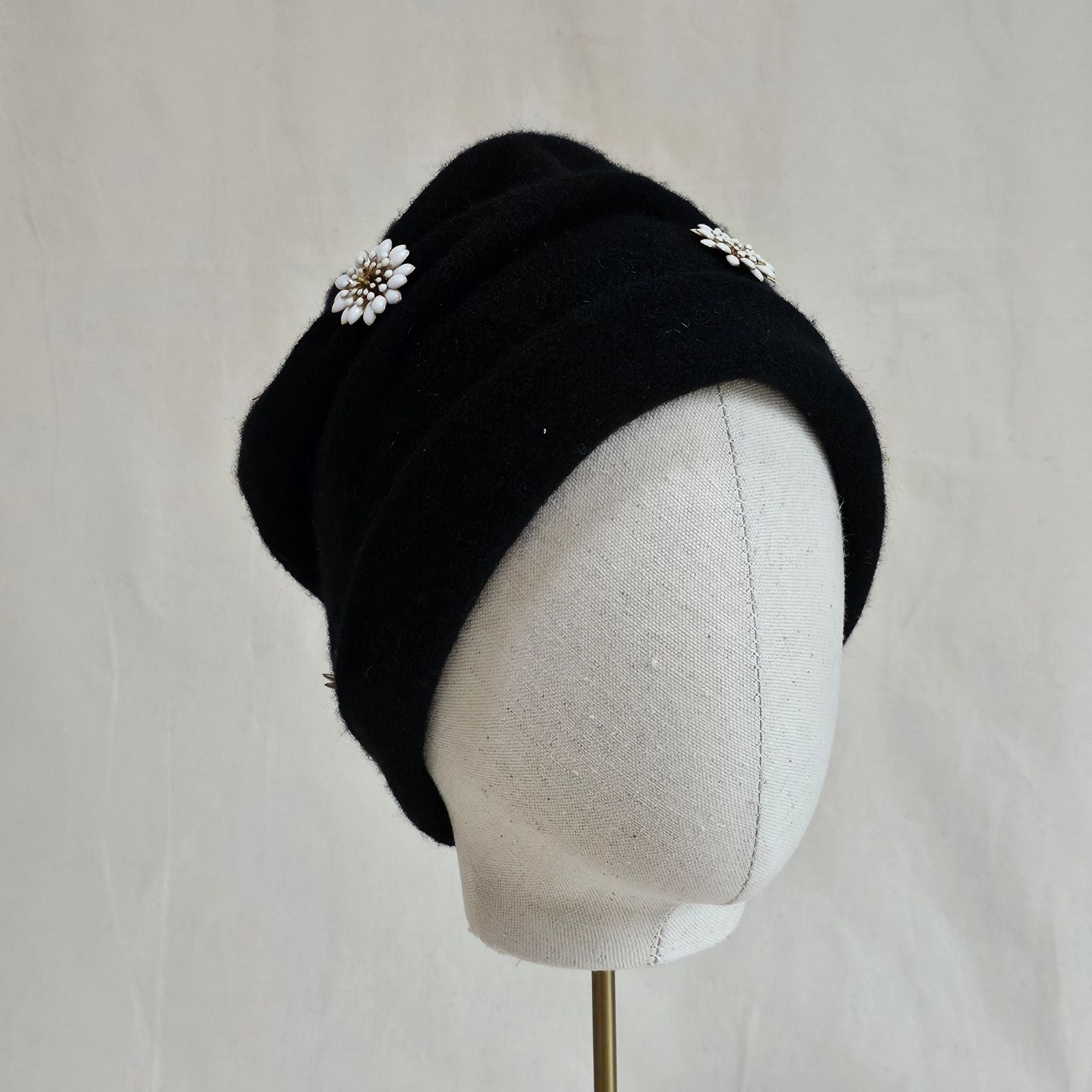 Black wool beanie with beautiful white daisy embellishments, angle view.