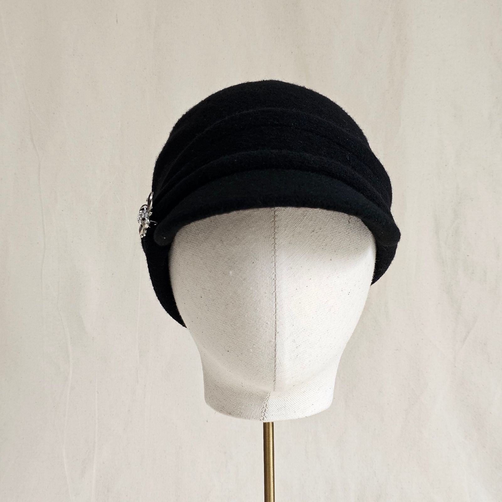 Black wool peak cap with beautiful brooch, front view.