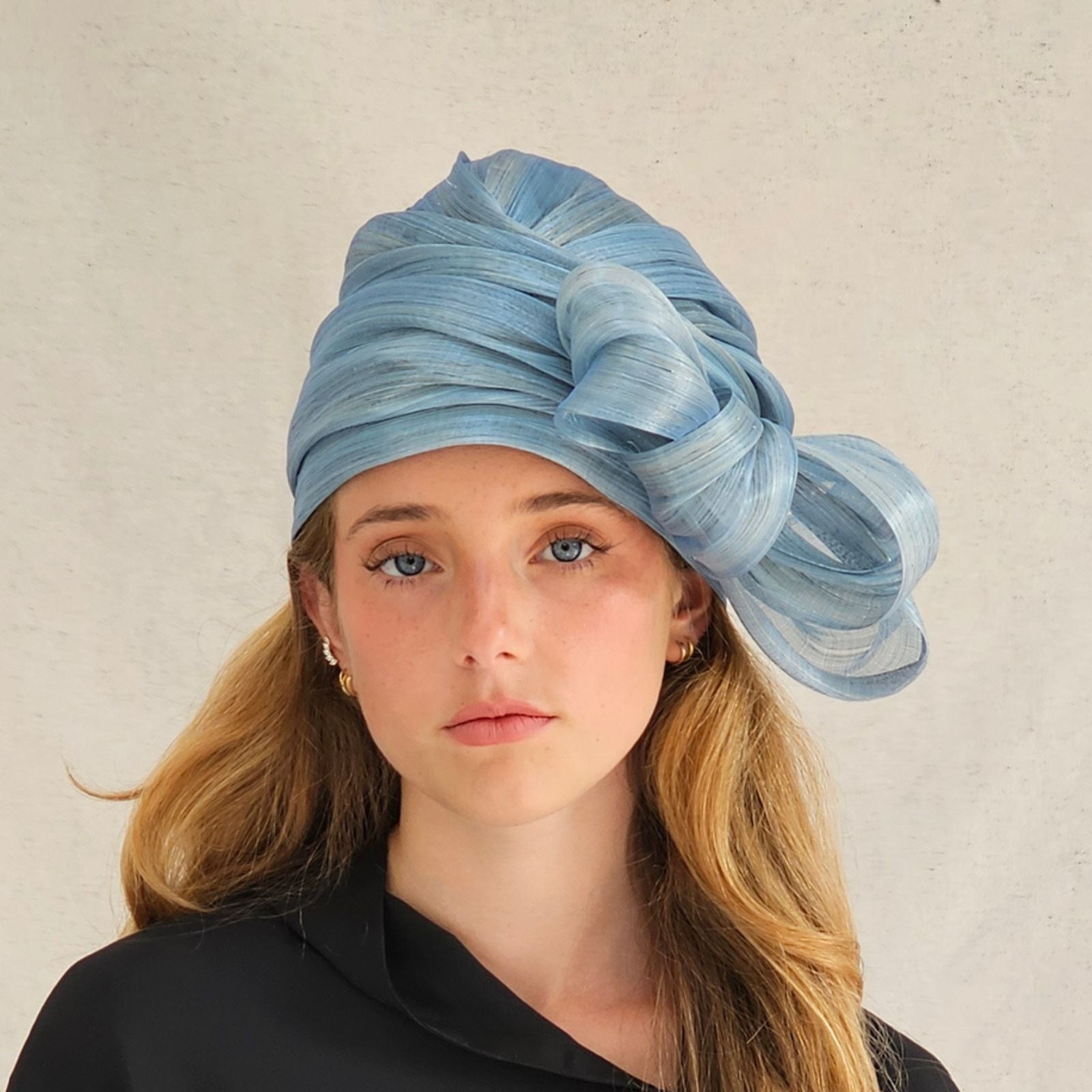 Blue silk abaca turban cloche moulded into elegant bow swirl, front view.
