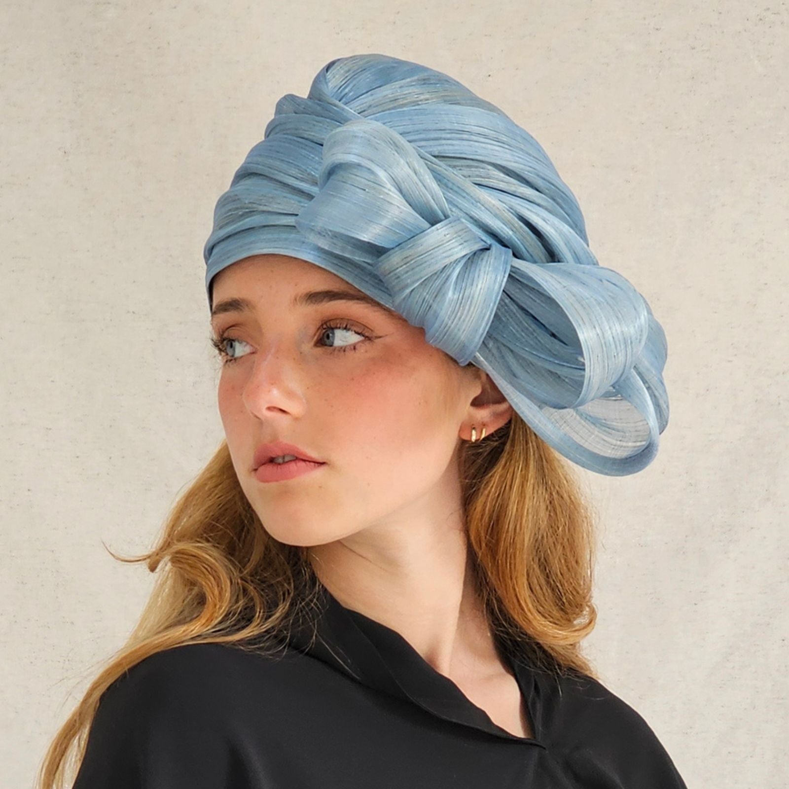 Blue silk abaca turban cloche moulded into elegant bow swirl, side view.