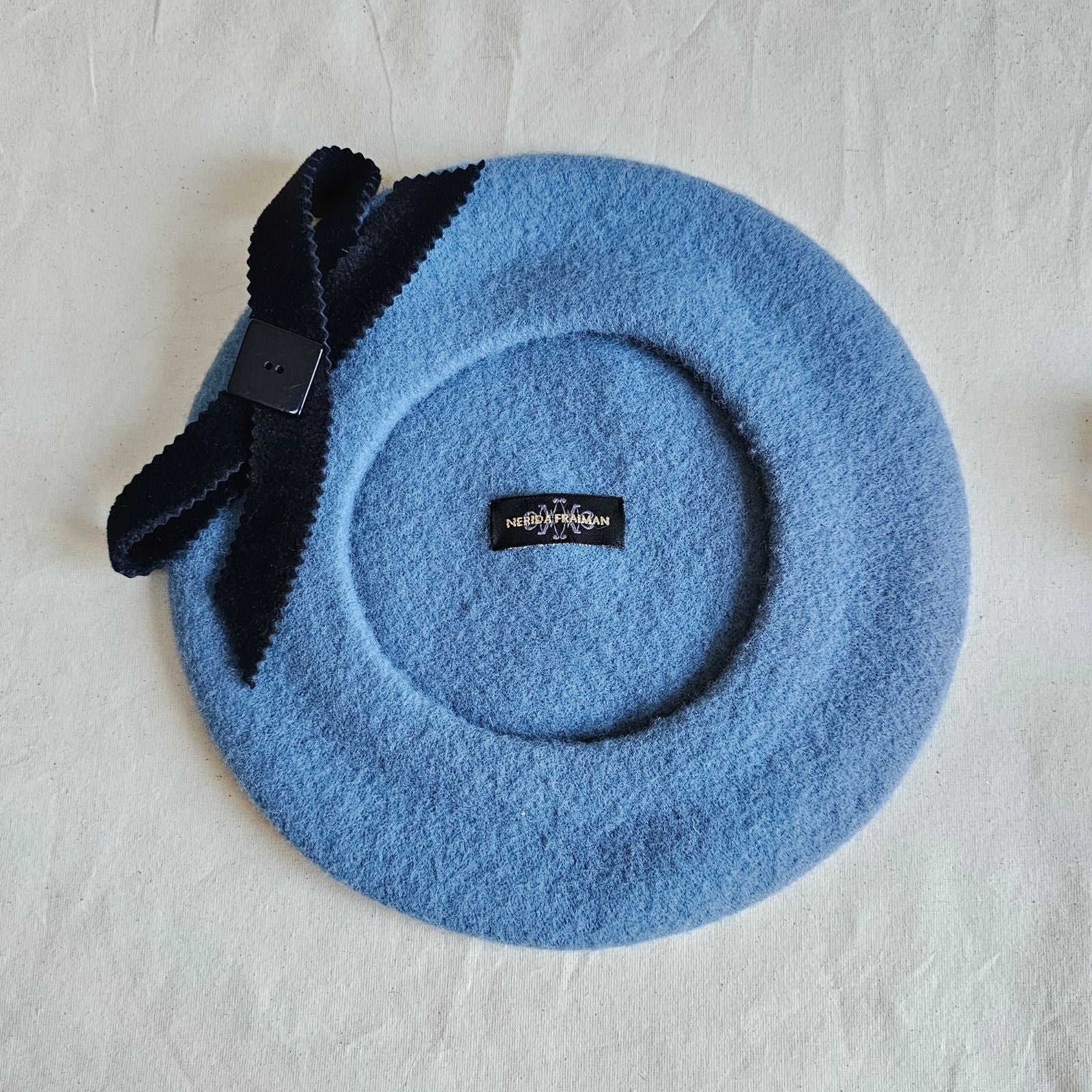 Blue wool beret with black bow embellishment, underside view.