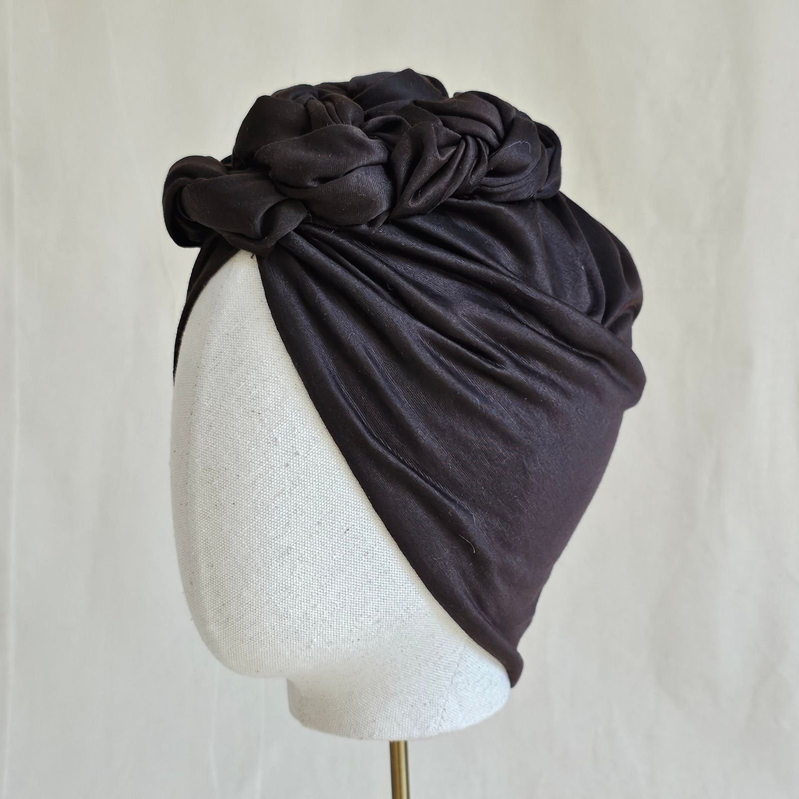 Brown cotton turban loosely gathered into intricate braid design, left view.