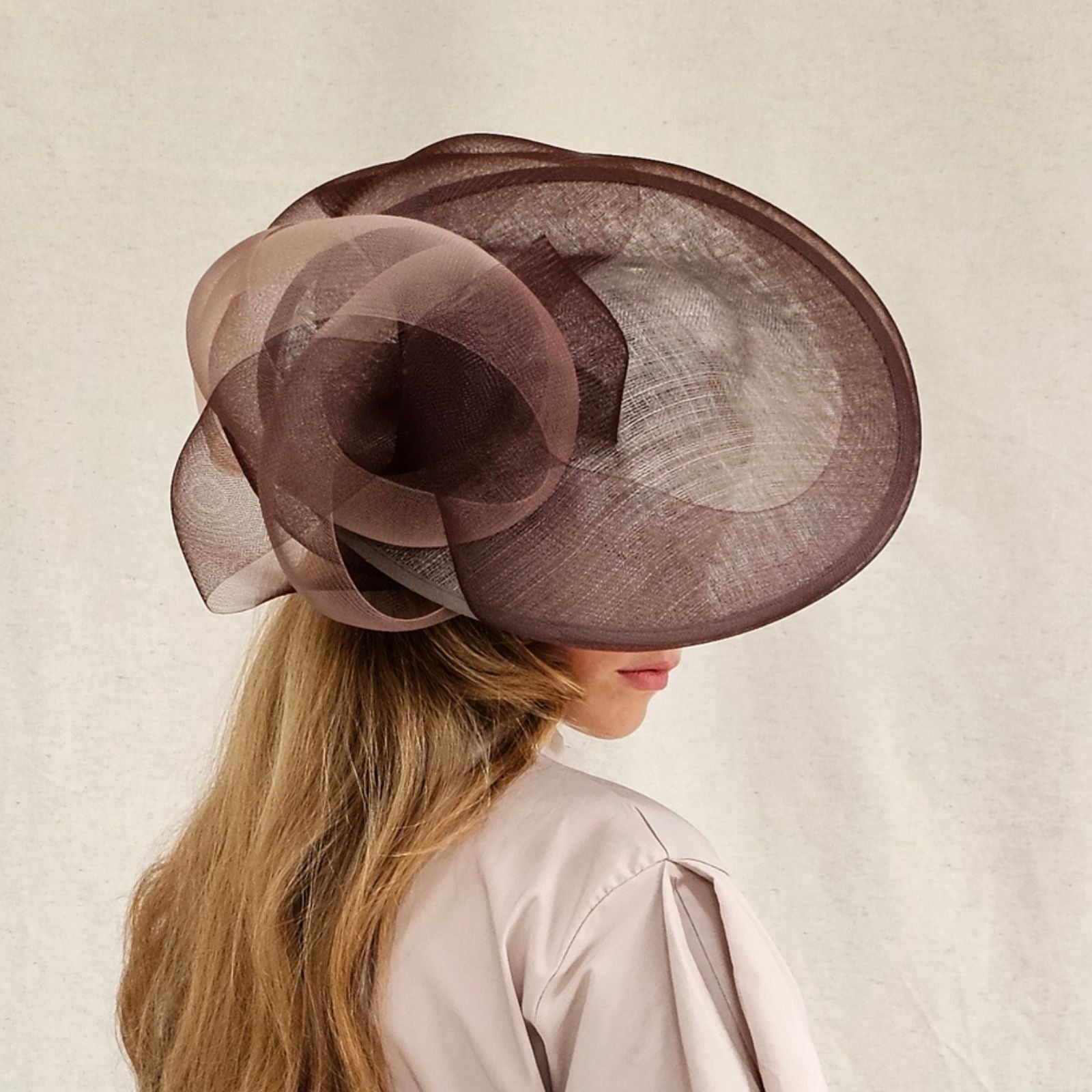 Brown sinamay disc hat with elegant crin bow swirl, side view.