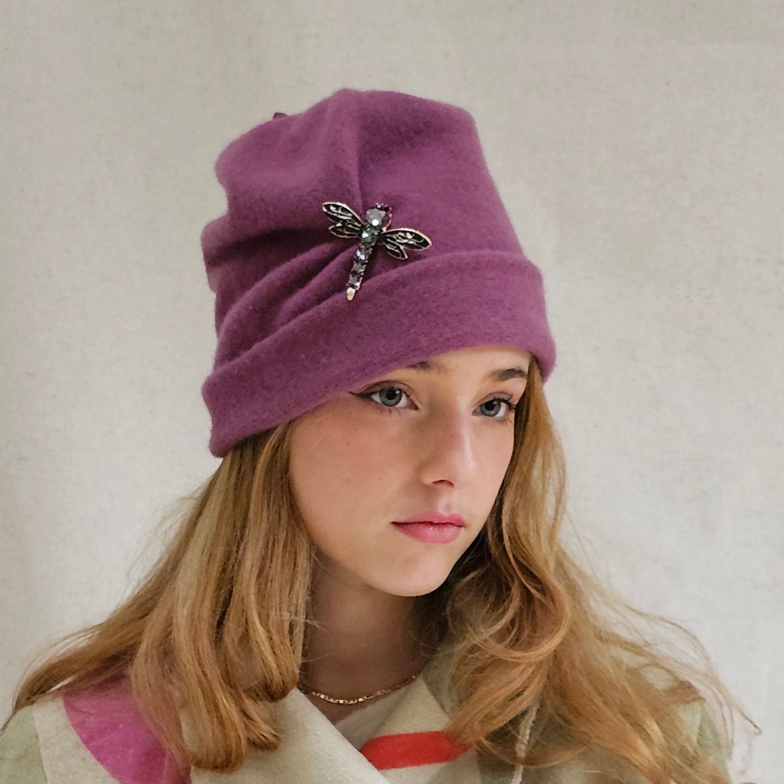 Dusky pink wool beanie with beautiful dragonfly brooch, angle view.