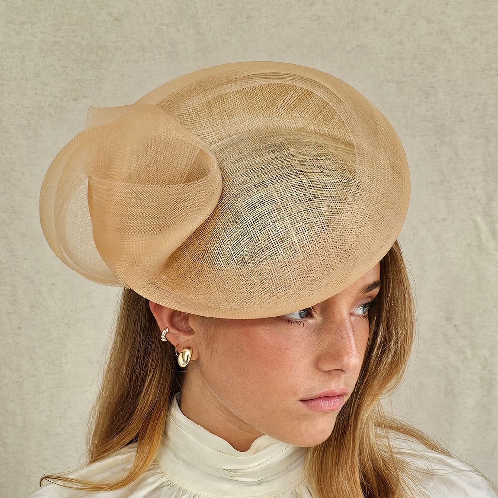 Golden straw disc hat with elegant crin knotted swirl, angle view.