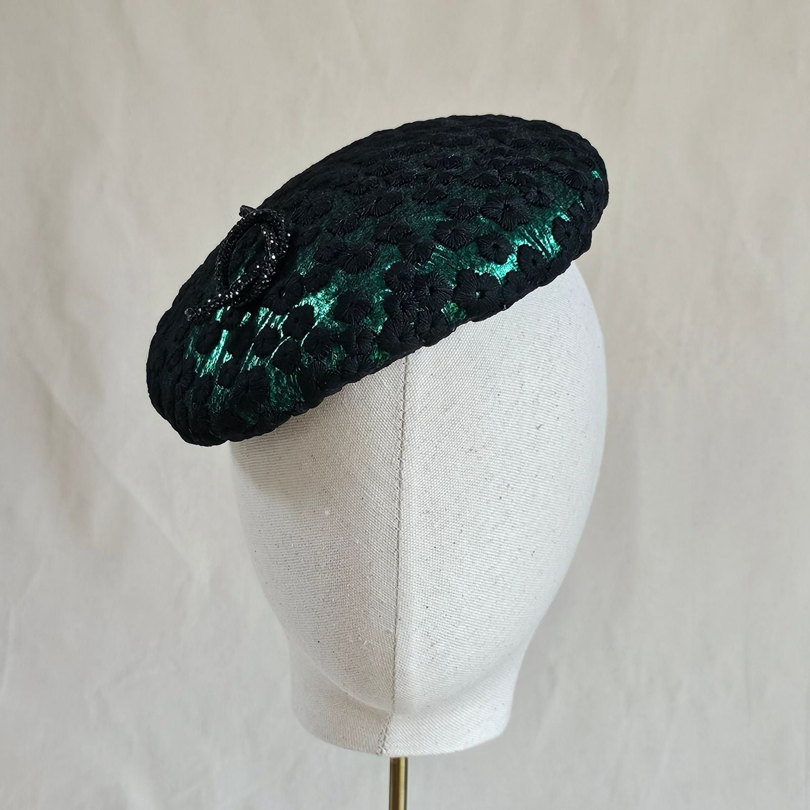 Emerald green beret with black flower lace and elegant brooch embellishment, front view.