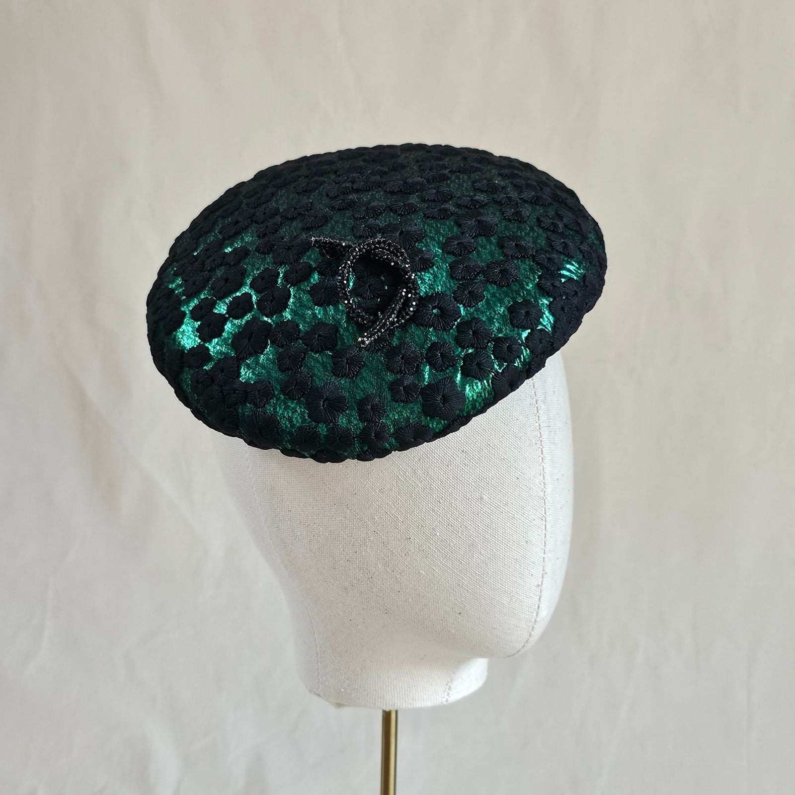 Emerald green beret with black flower lace and elegant brooch embellishment, right angle view.