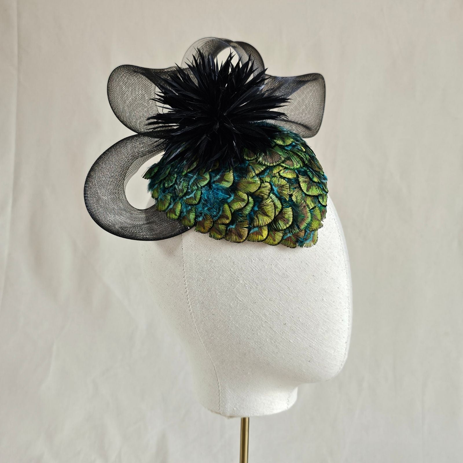 Green peacock feather hat with black feather flower and elegant crin swirl, left view.