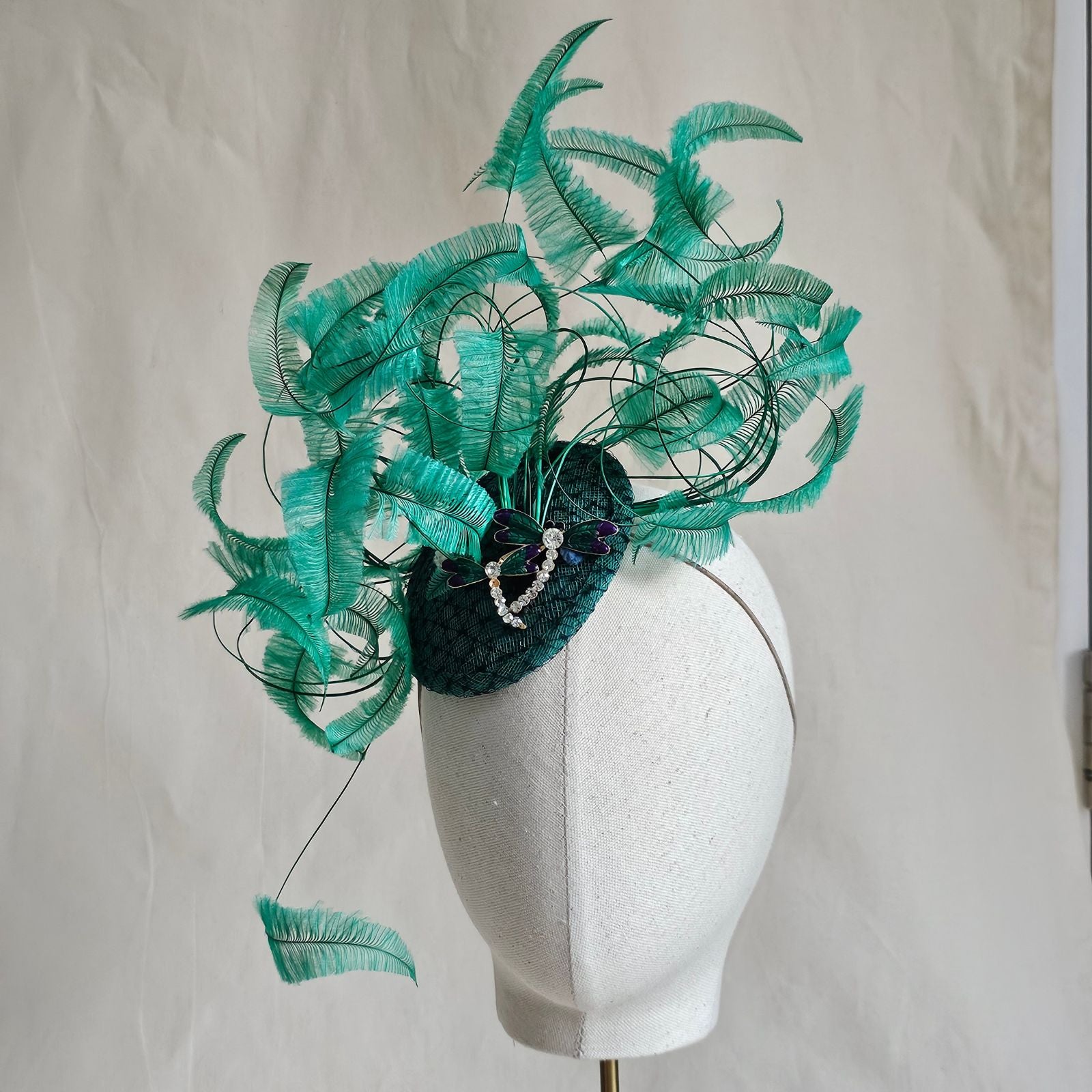 Green fascinator with elegant curled feathers and beautiful dragonfly embellishments, left view.