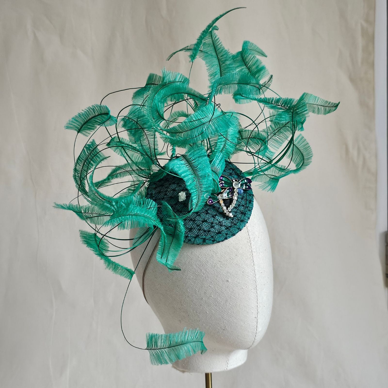 Green fascinator with elegant curled feathers and beautiful dragonfly embellishments, right view.