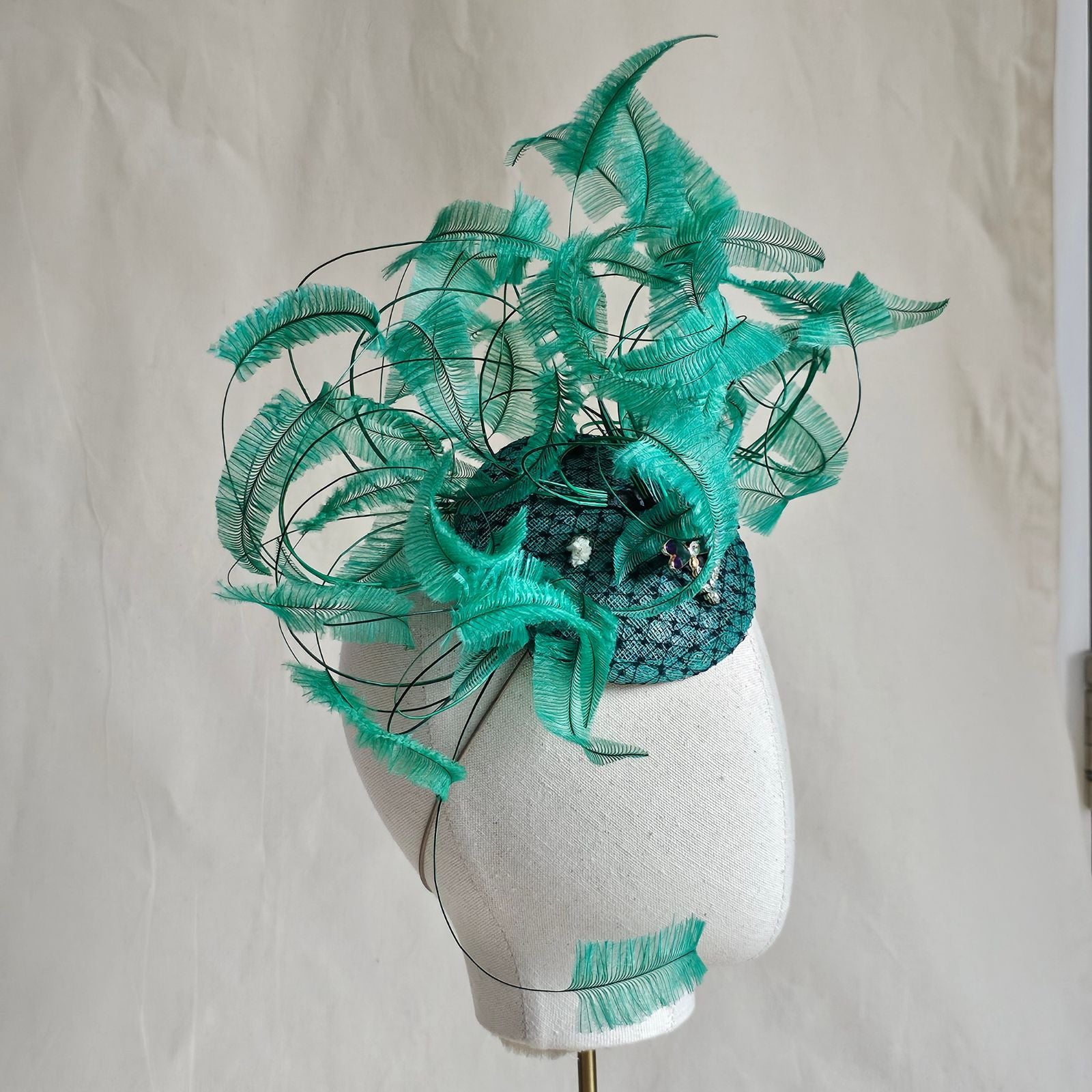 Green fascinator with elegant curled feathers and beautiful dragonfly embellishments, side view.