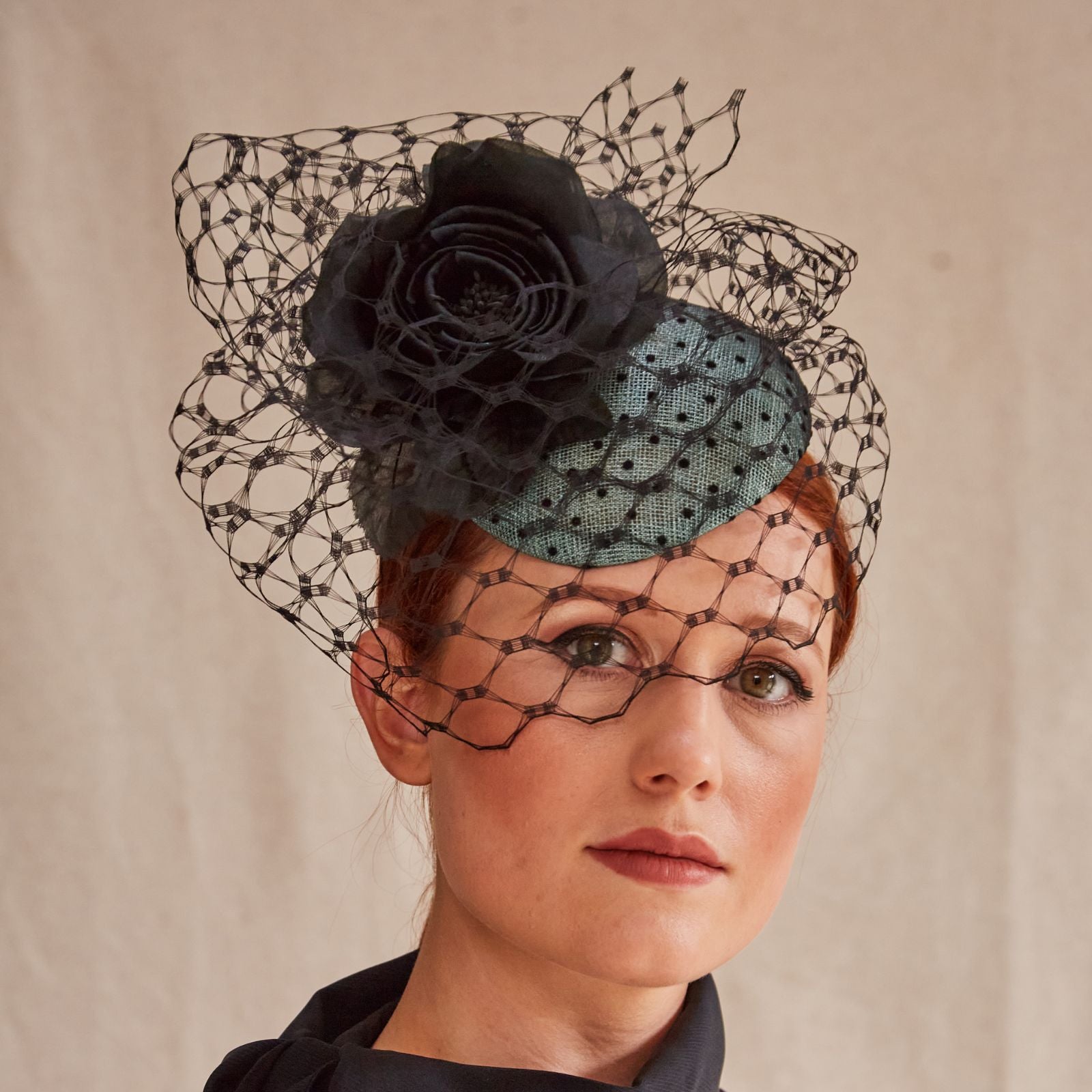 Green sinamay beret with intricate black veiling and flower embellishment, angle view.
