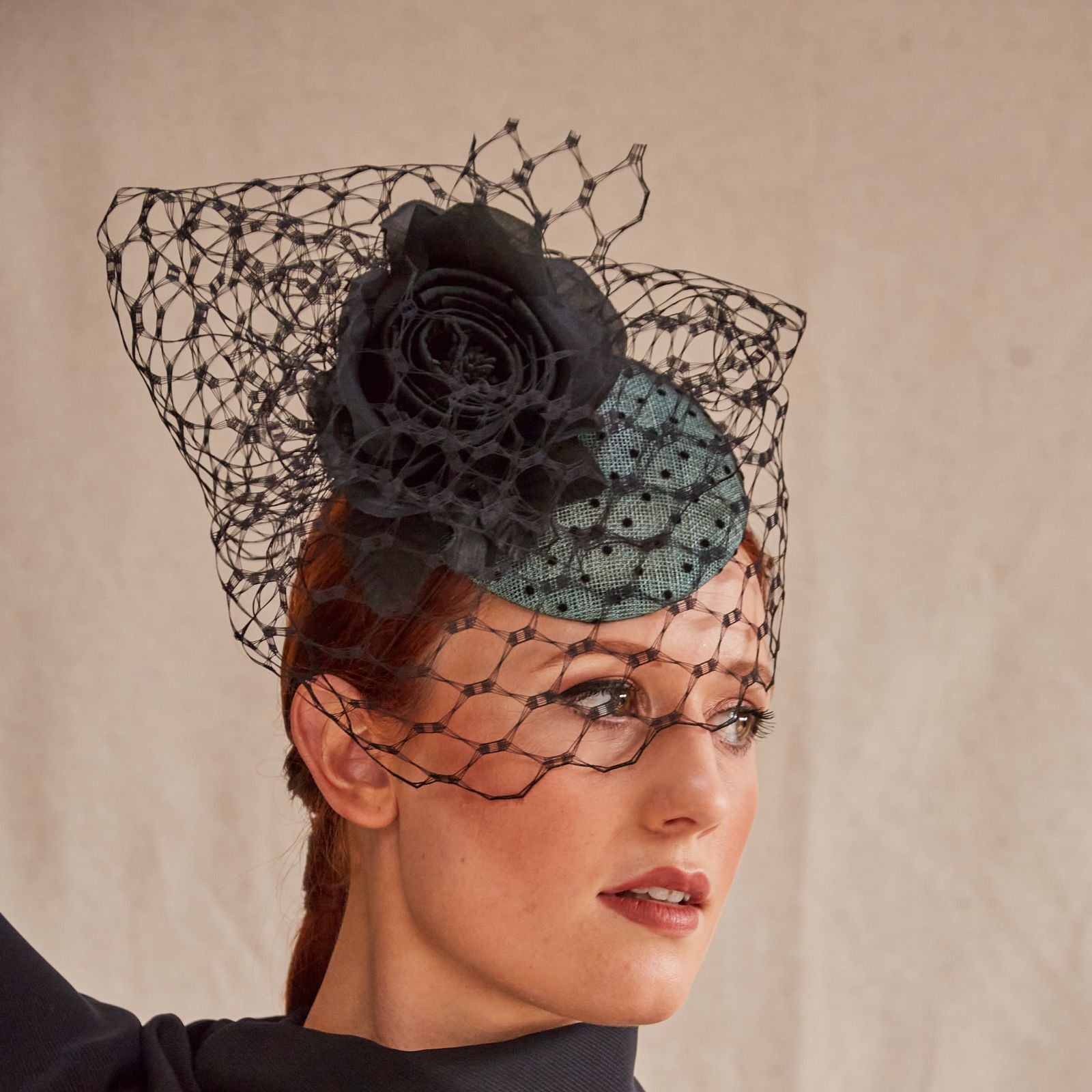 Green sinamay beret with intricate black veiling and flower embellishment, side view.