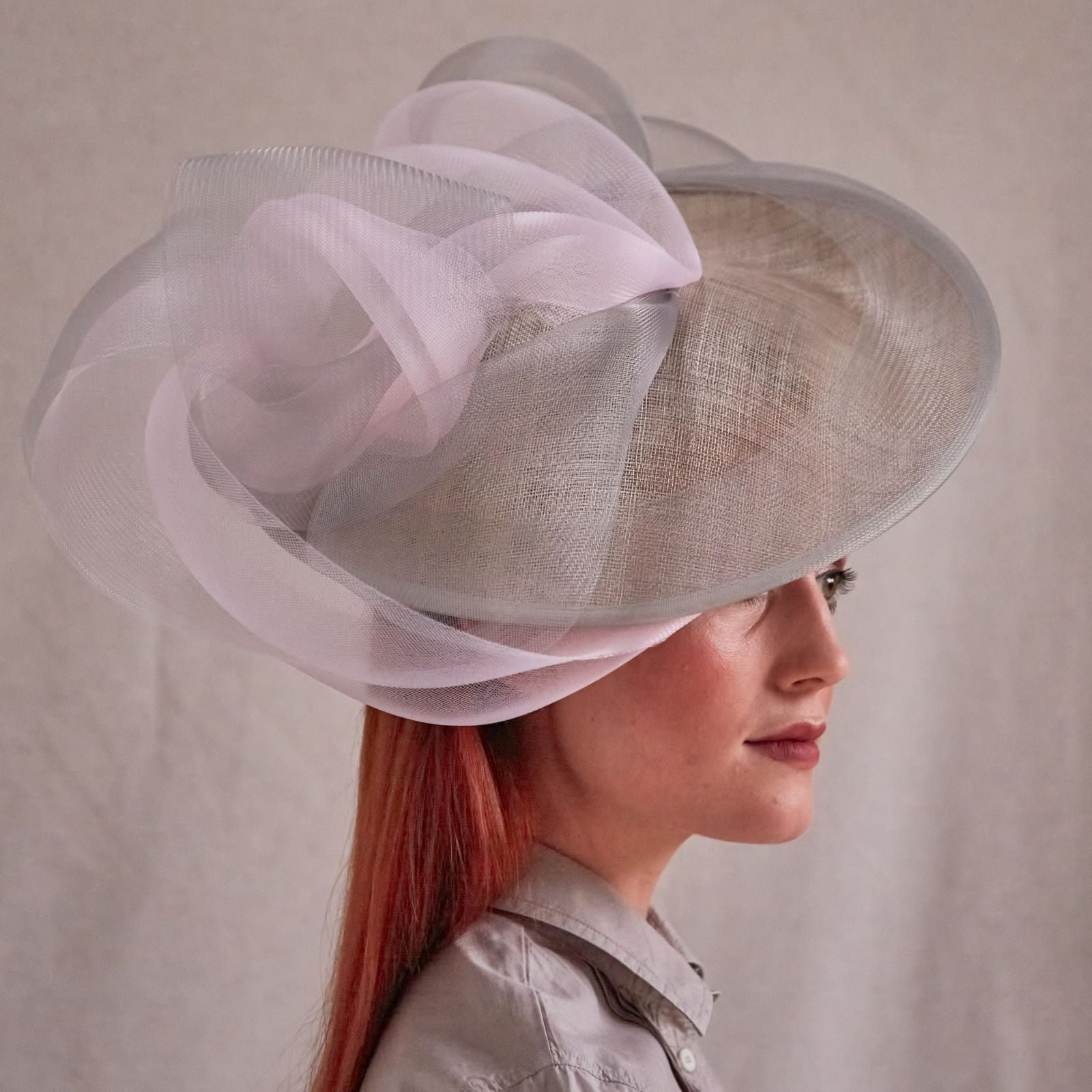 Grey and pink sinamay disc hat with elegant crin swirls, side view.