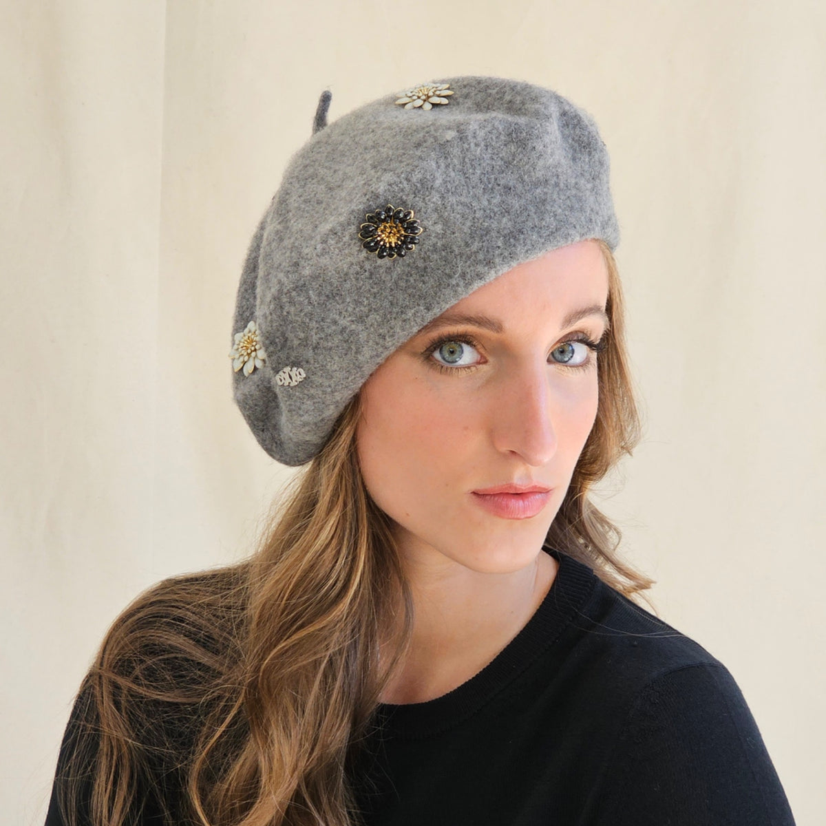Grey wool beret with flower and monogram embellishments, worn
tilted on a model.
