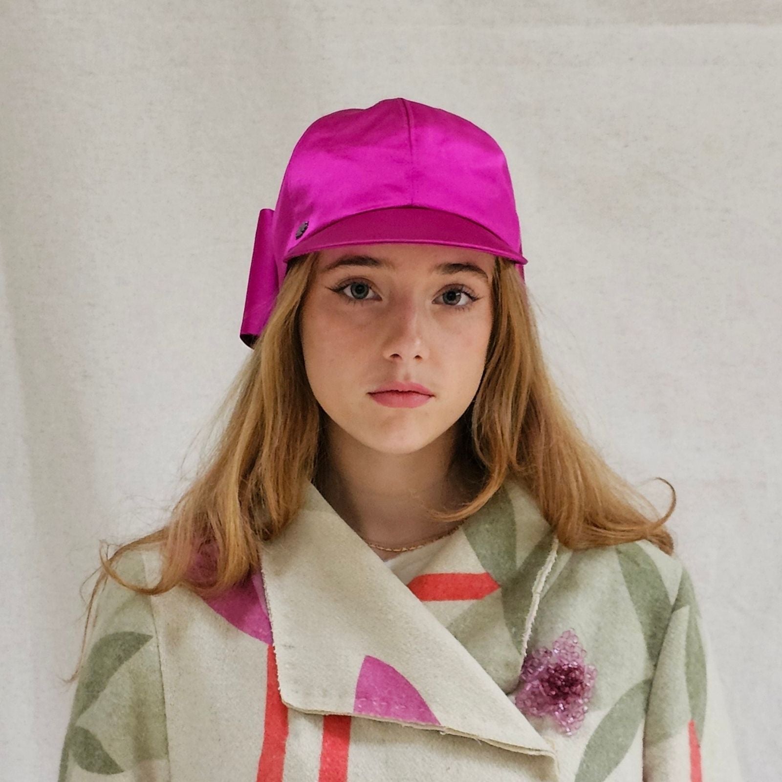 Hot pink silk baseball cap with dramatic bow, front view.