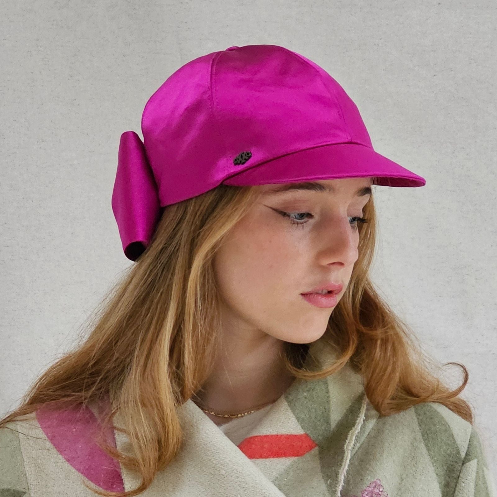 Hot pink silk baseball cap with dramatic bow, side view.
