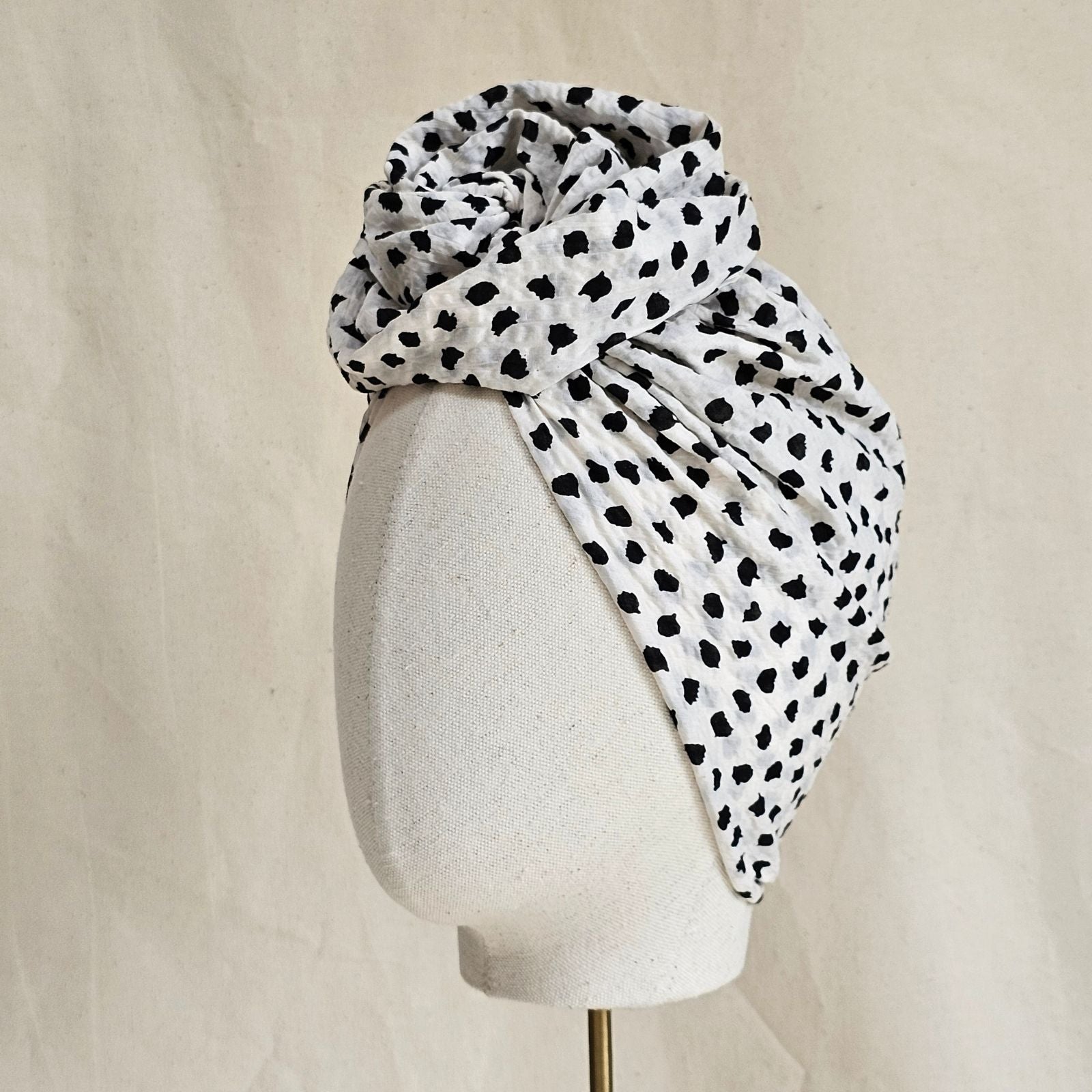 Ivory cotton turban with black dot print loosely gathered into beautiful sculptural knotted rose, side view.