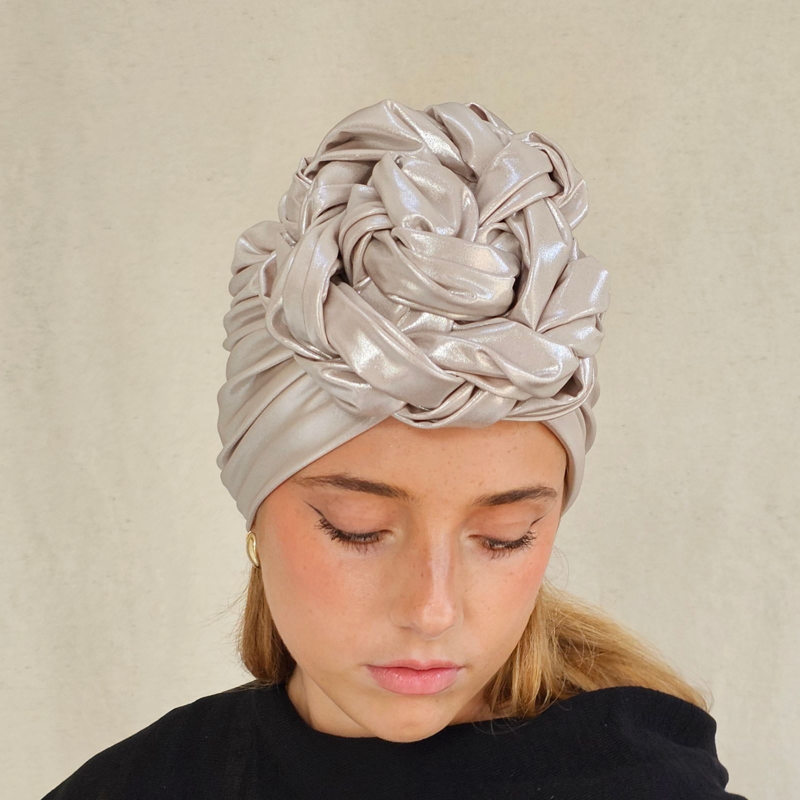 Ivory sparkly designer turban gathered into intricately plaited flower knot, angle view.