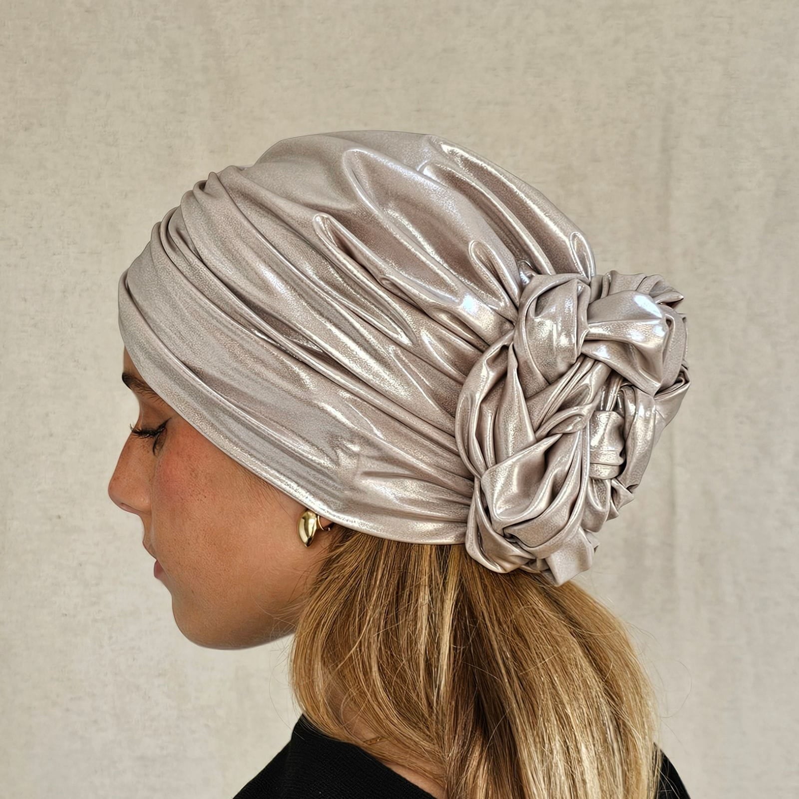 Ivory sparkly designer turban gathered into intricately plaited flower knot, side view.