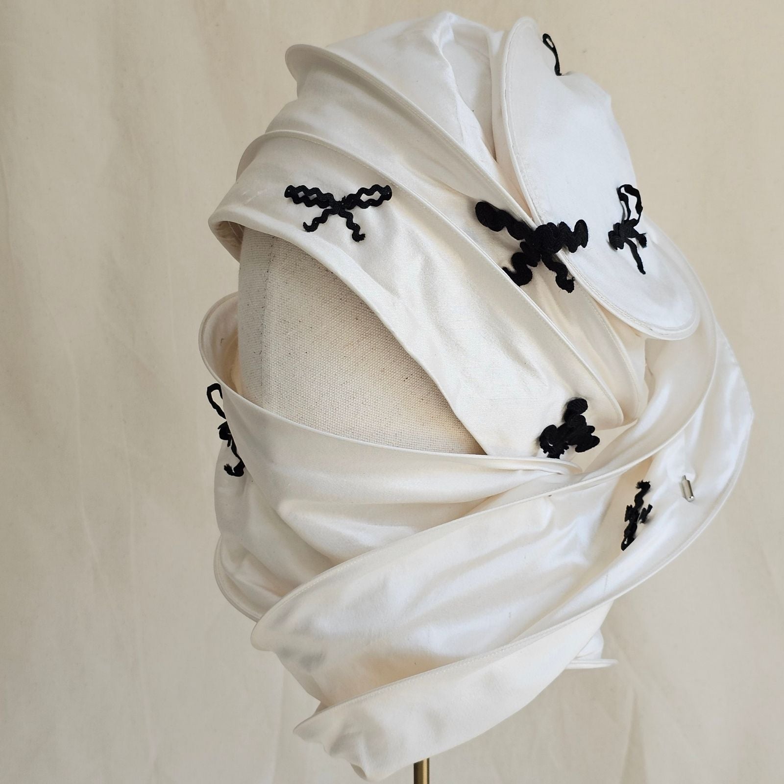 Ivory silk scarf turban with black bow detailing, left view.