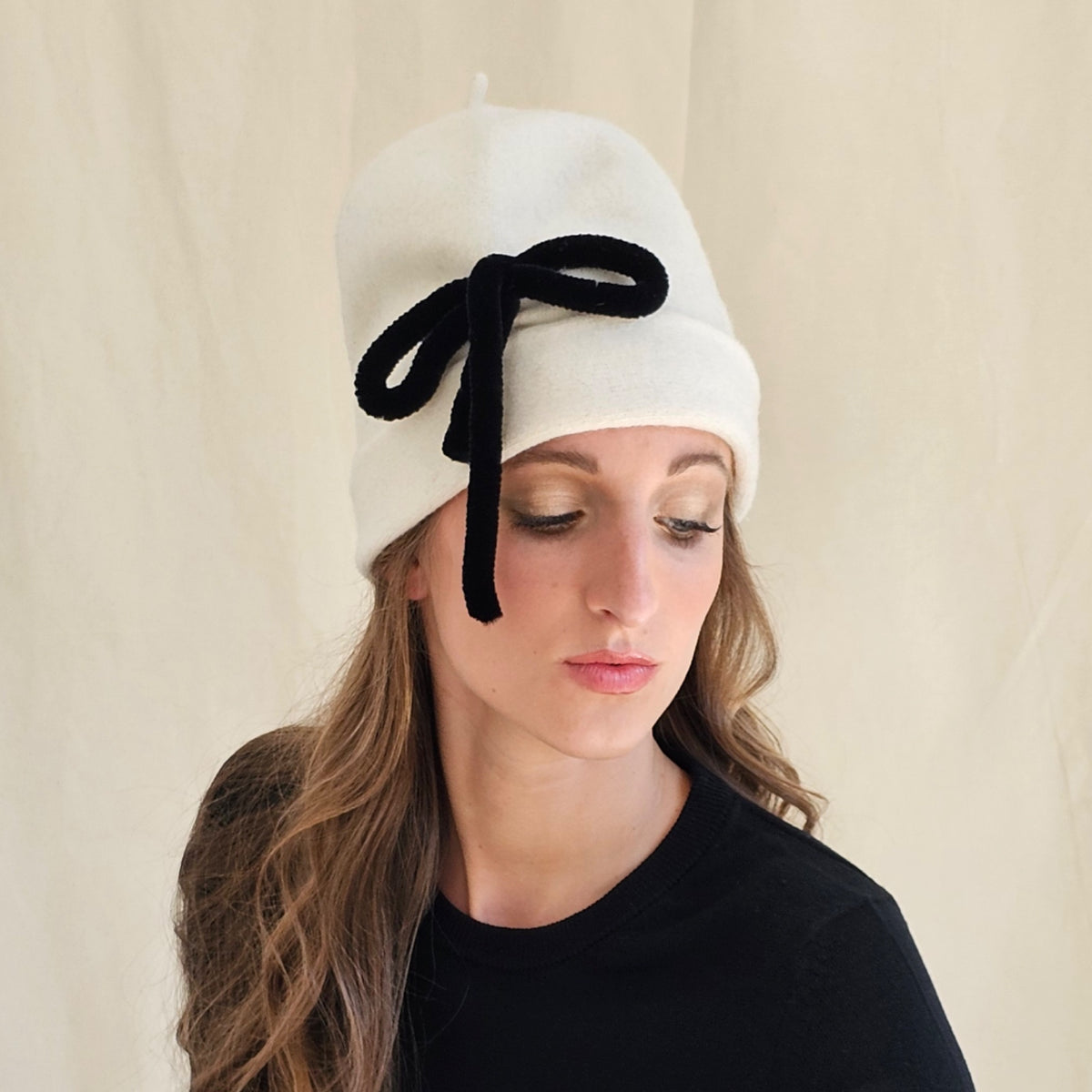 Ivory gathered wool beanie with a black bow, worn on a model.