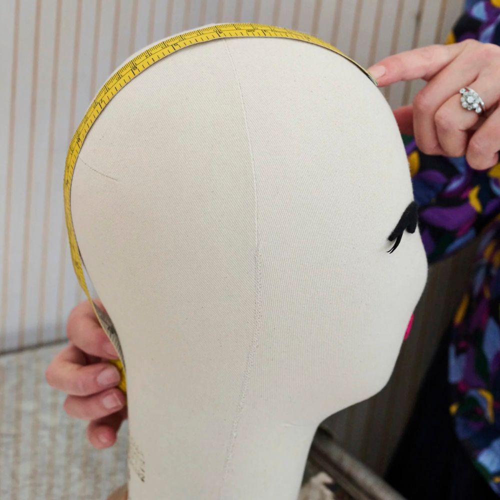 Mannequin head with measuring tape, used for head sizing for fashion or design purposes.