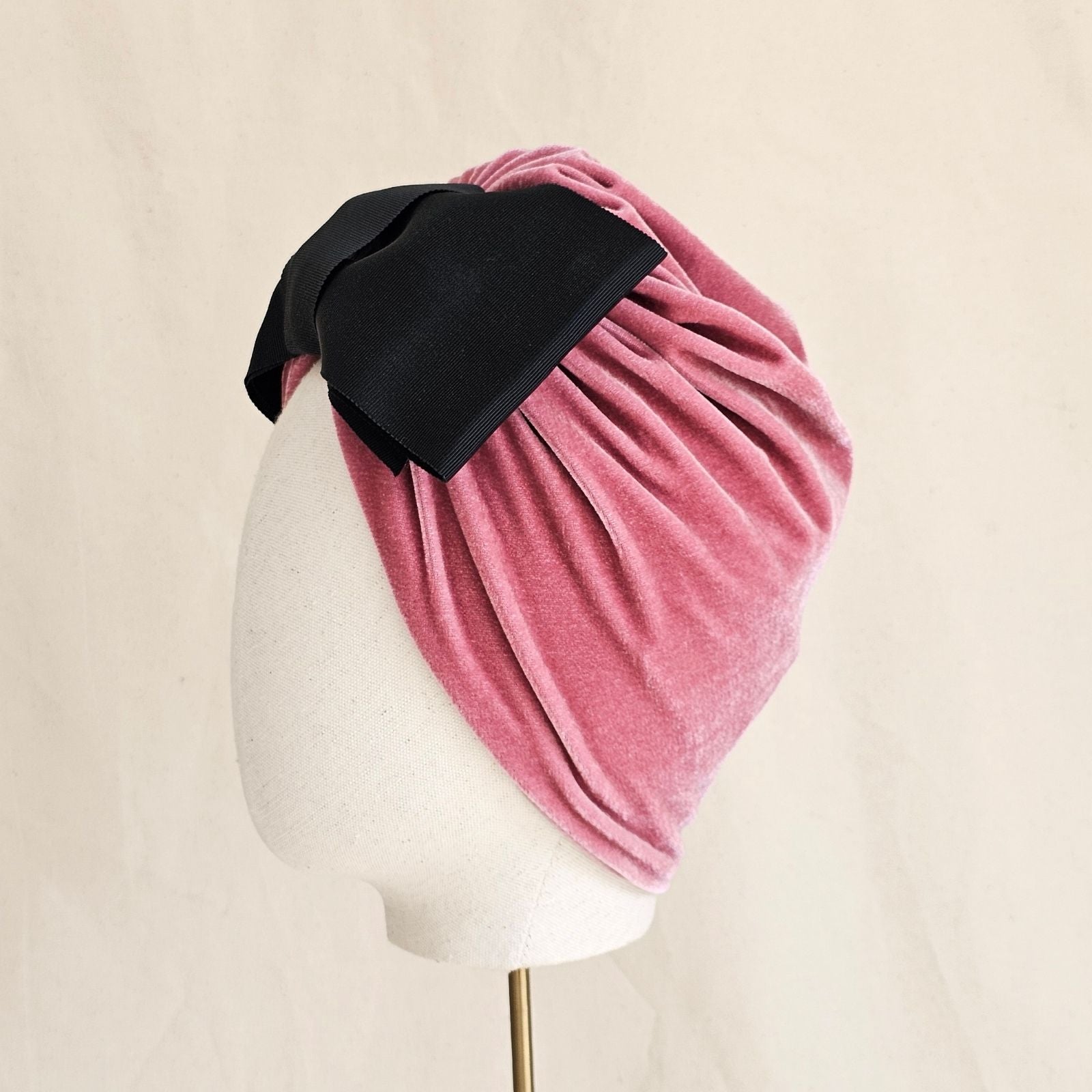 Pink velvet turban loosely gathered with dramatic black bow, left view.