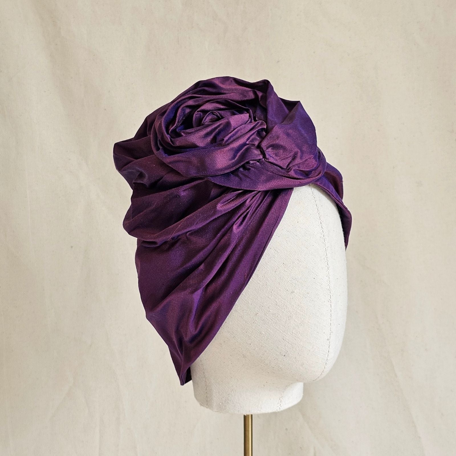 Purple silk turban gathered into intricately sculpted rose knot, angle view.