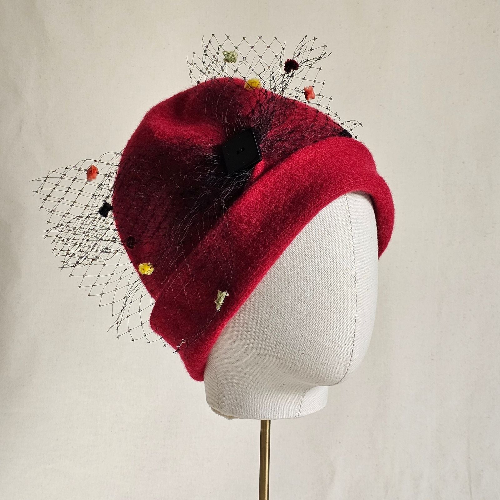 Red wool beanie with multicoloured spot veiling bow, angle view.
