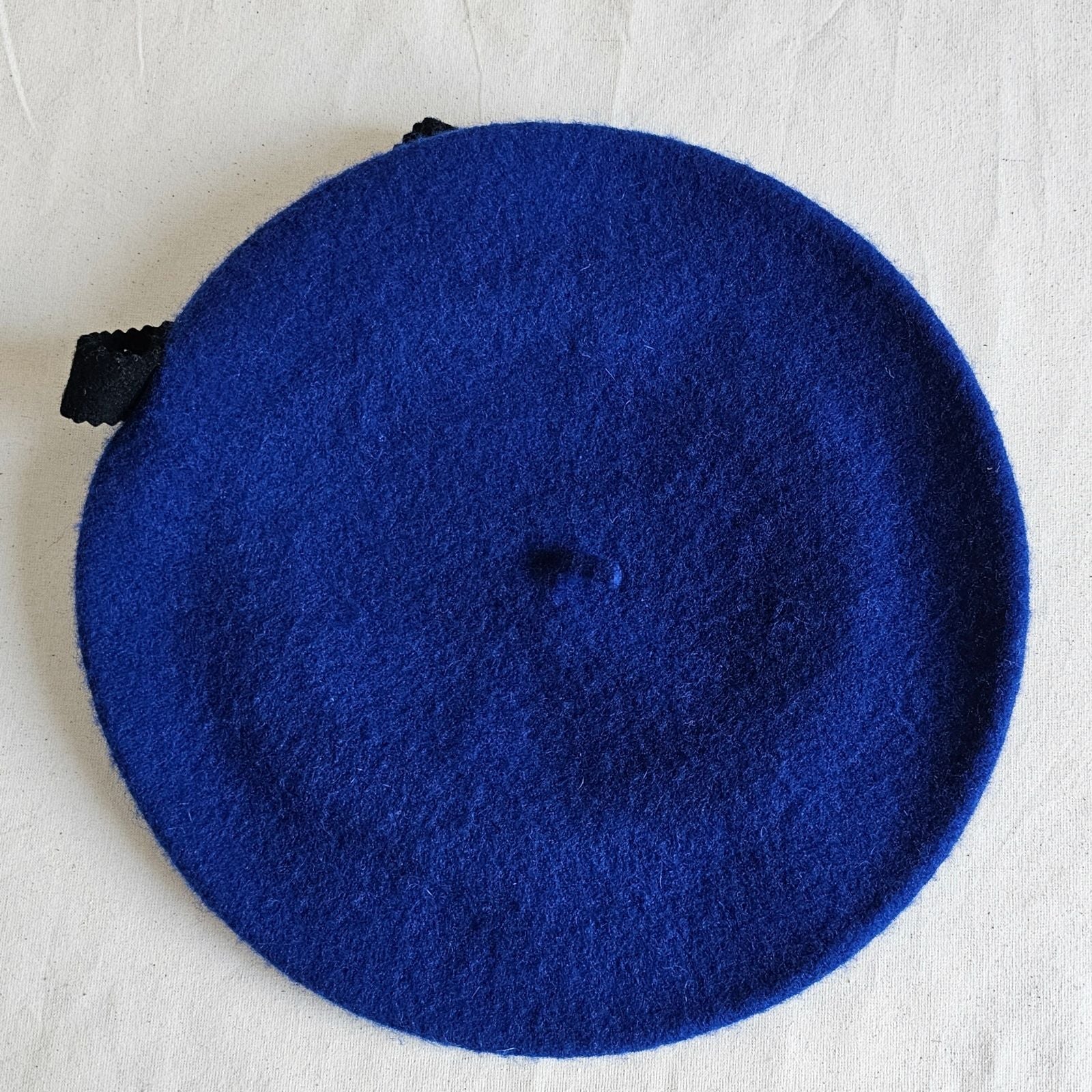 Royal blue wool beret with black bow embellishment, top view.