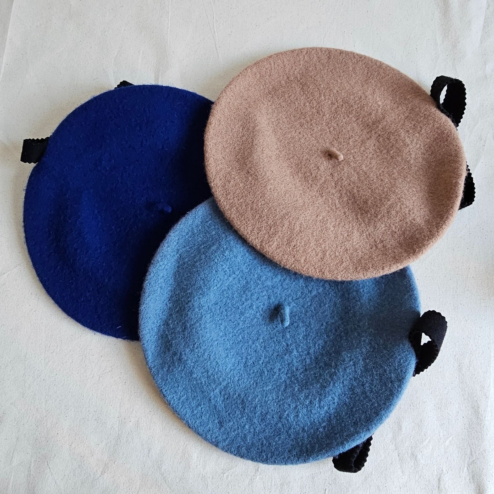 Tan, blue and royal blue wool berets with black bow embellishment, top view.