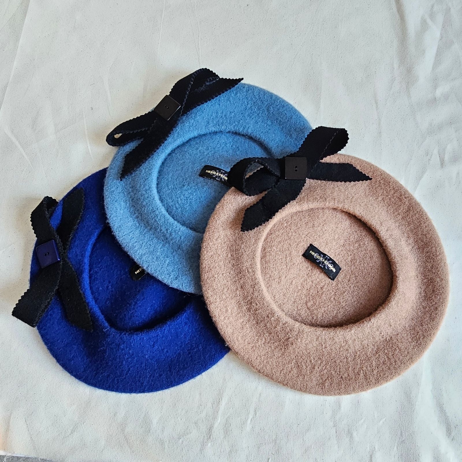 Tan, blue and royal blue wool berets with black bow embellishment, underside view.