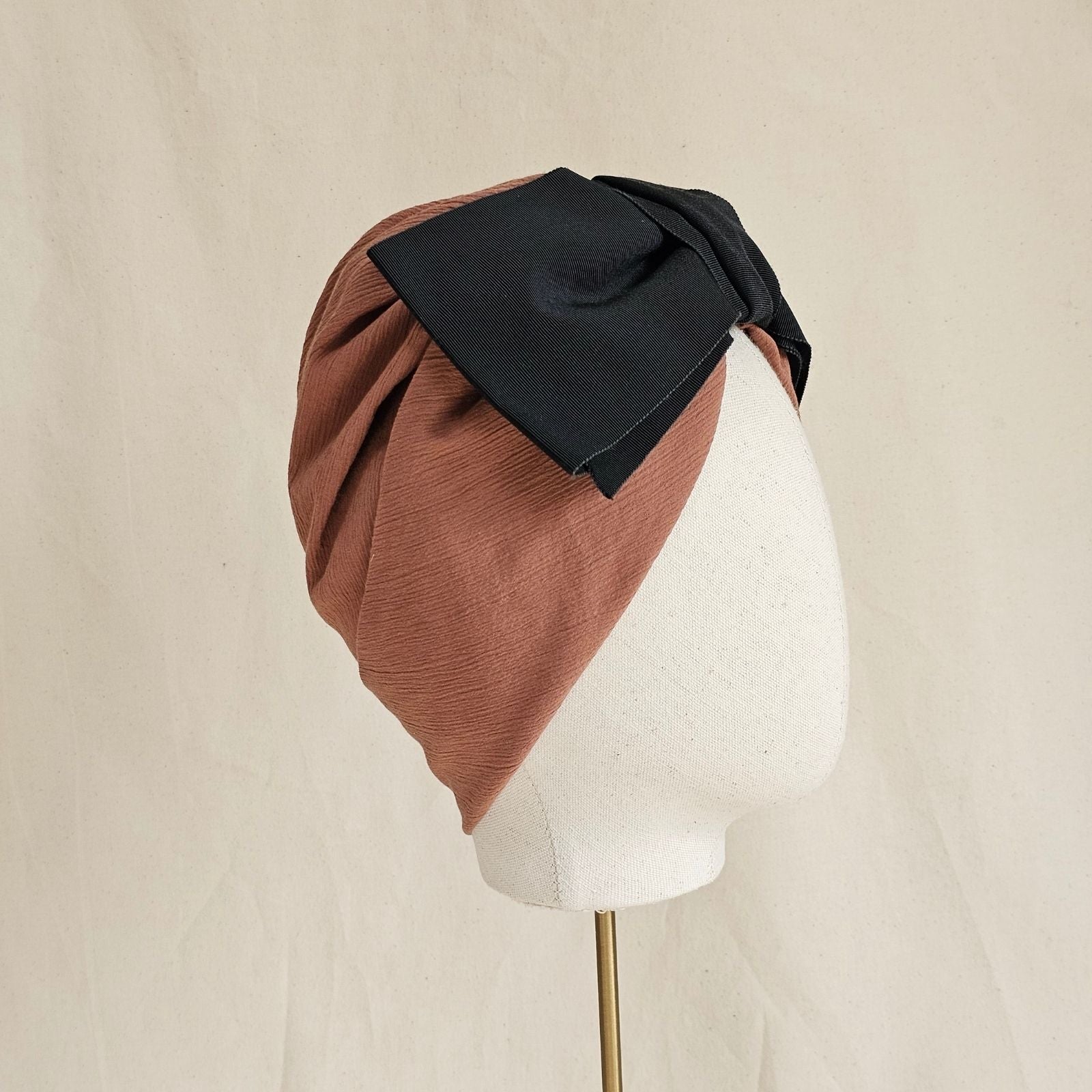 Tan cotton turban with dramatic black petersham bow, side view.