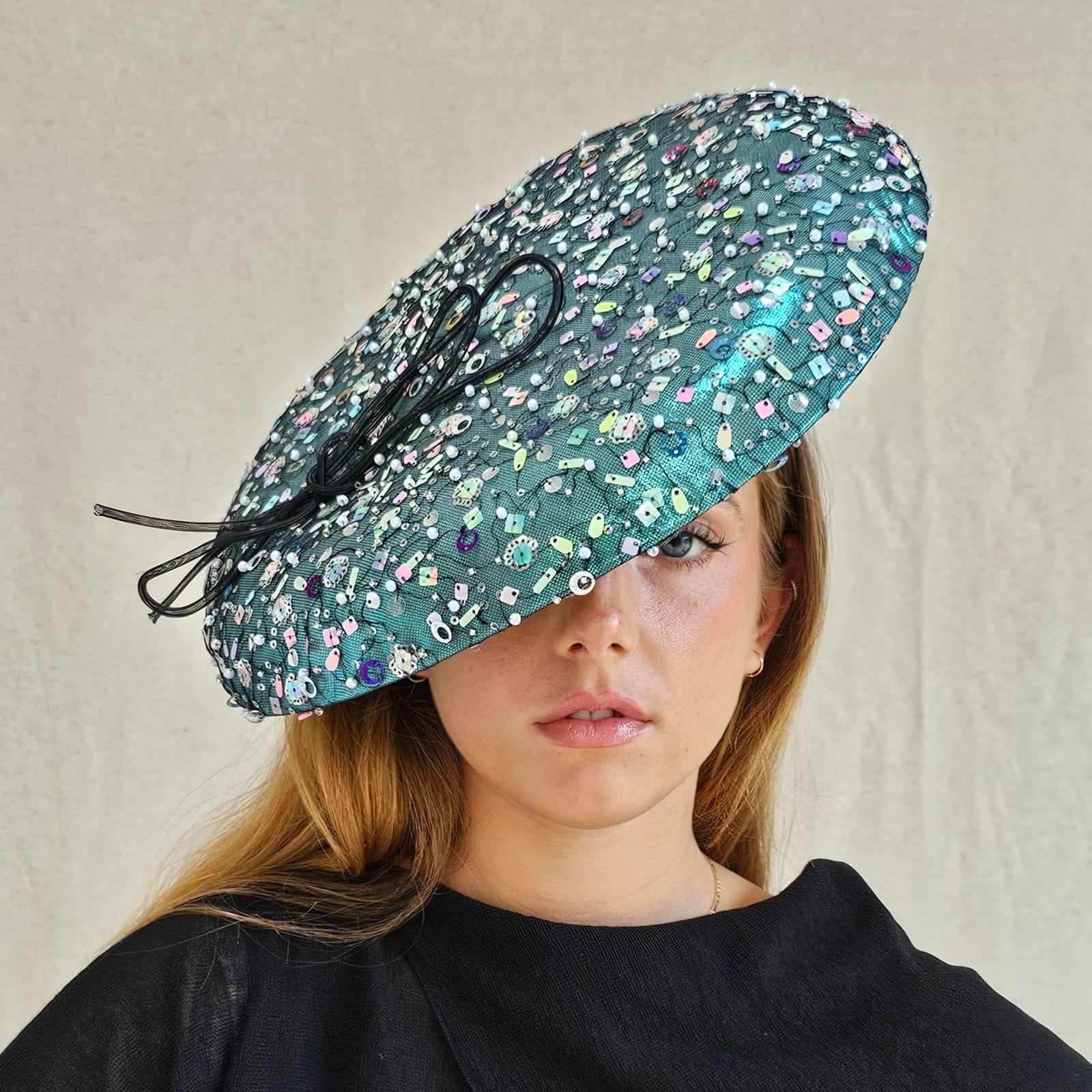 Aqua lamé disc hat with multicolour tulle sequining and elegant black bow, front view.