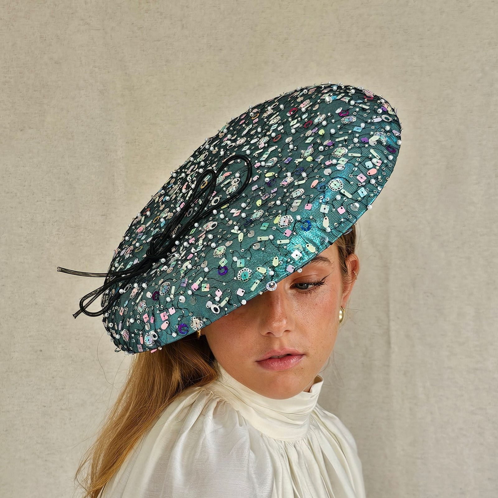 Aqua lamé disc hat with multicolour tulle sequining and elegant black bow, front view.