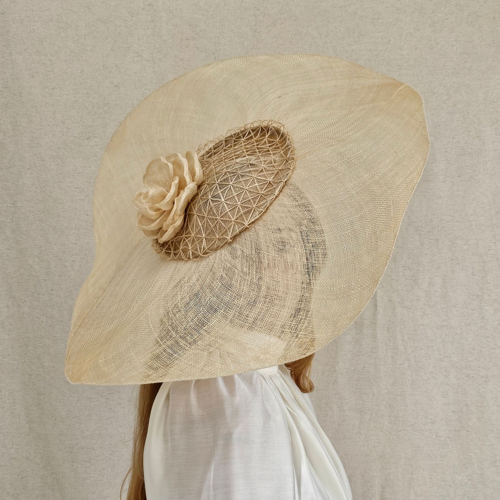Front view of model wearing natural sinamay Ascot disc hat with mesh veil and sculptural rose detail.
