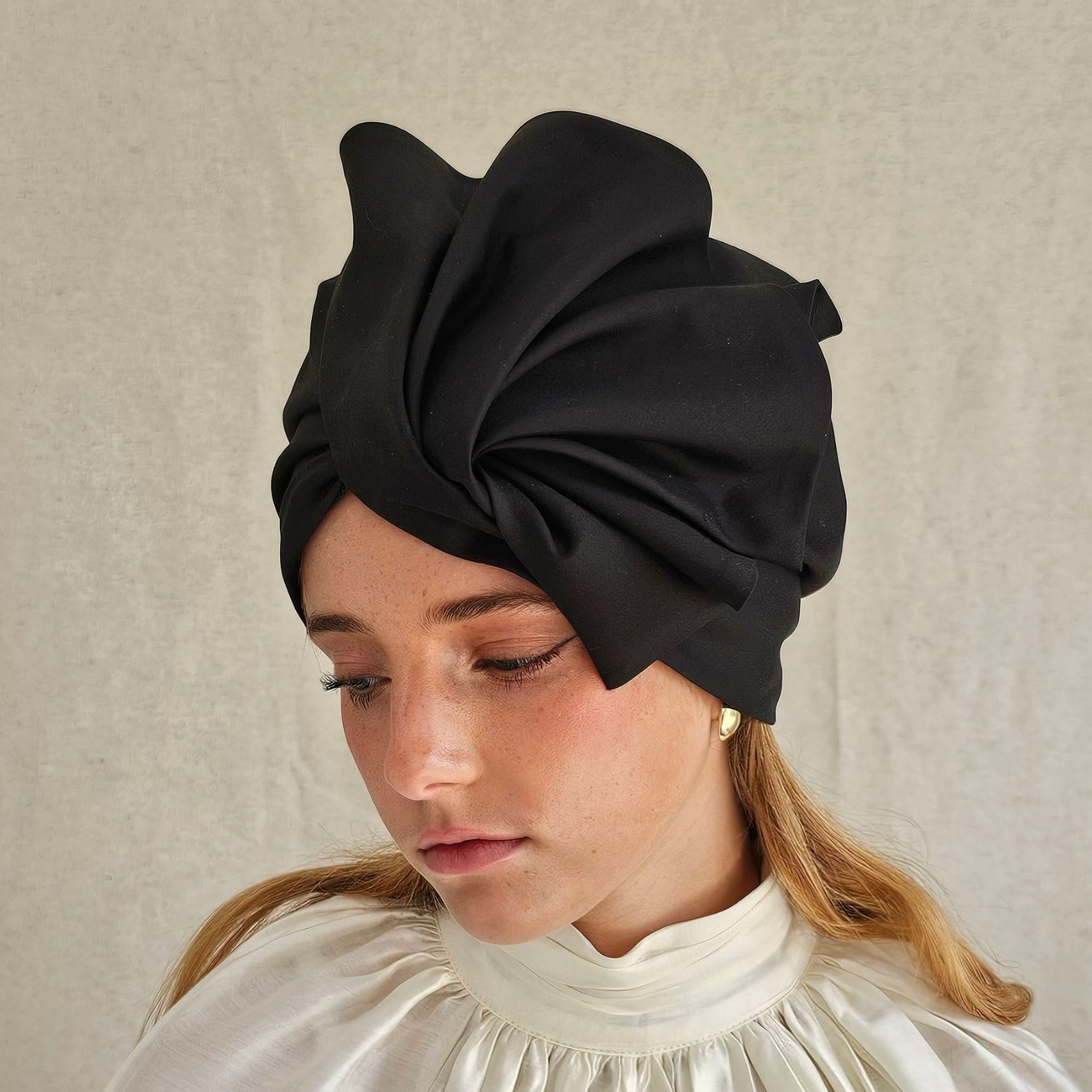 Black cotton turban with dramatic fold sculpting, side view.